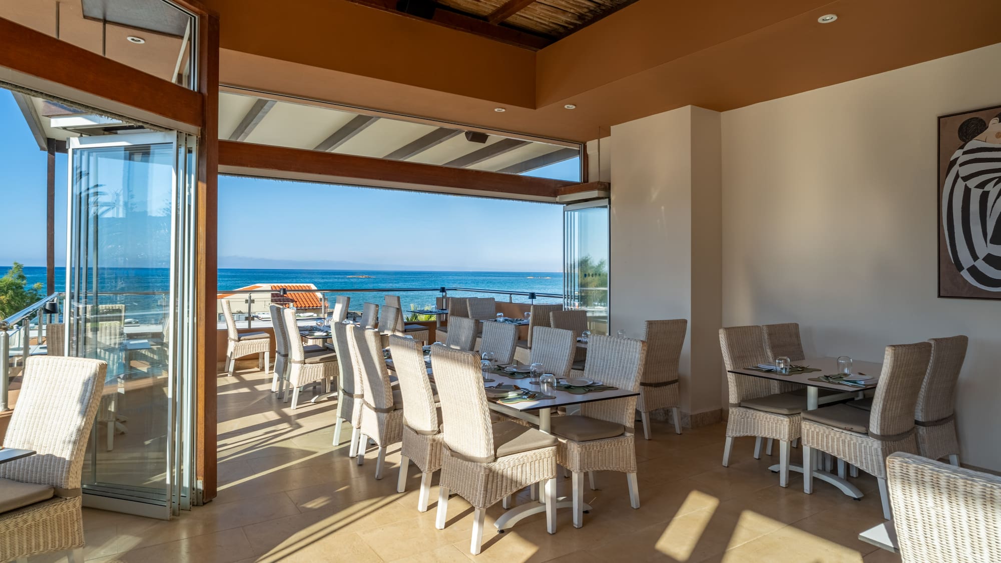 Open restaurant with ocean views, wicker dining chairs, and set tables.