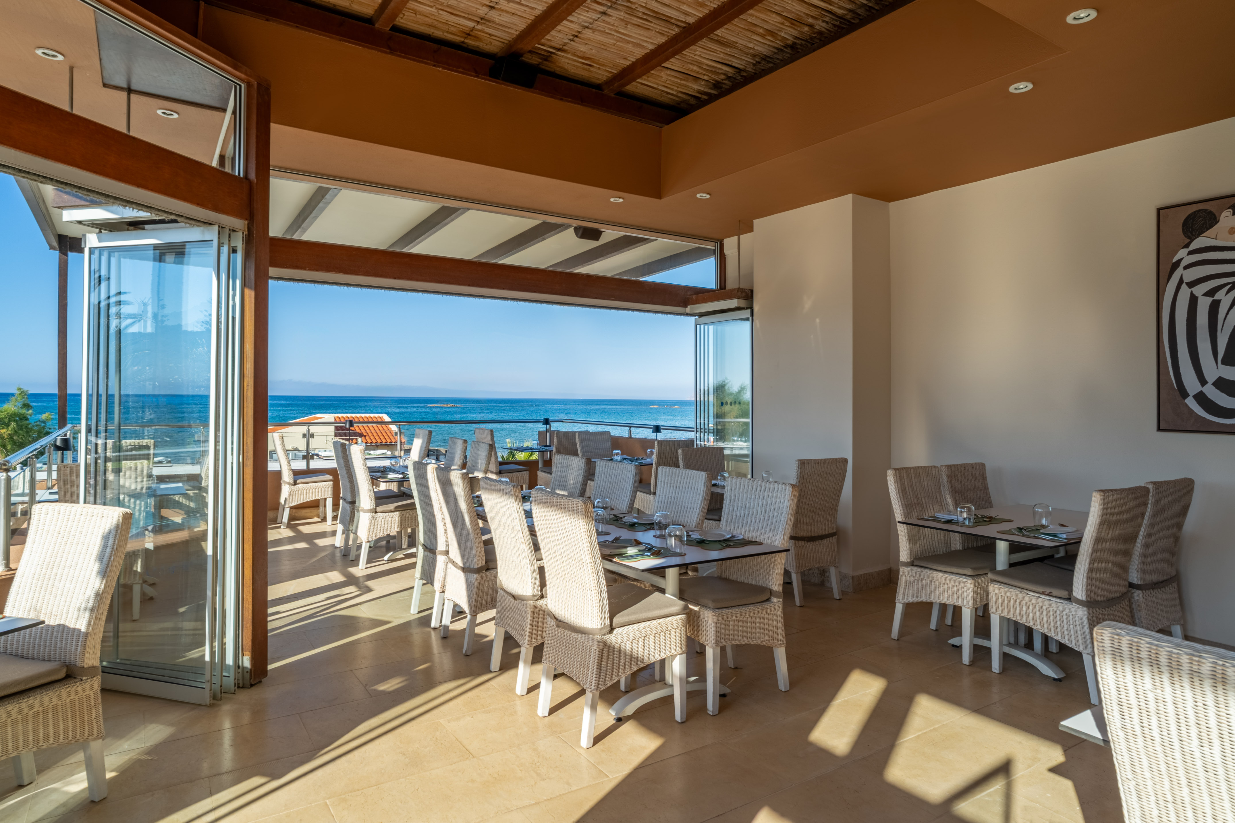 Open restaurant with ocean views, wicker dining chairs, and set tables.