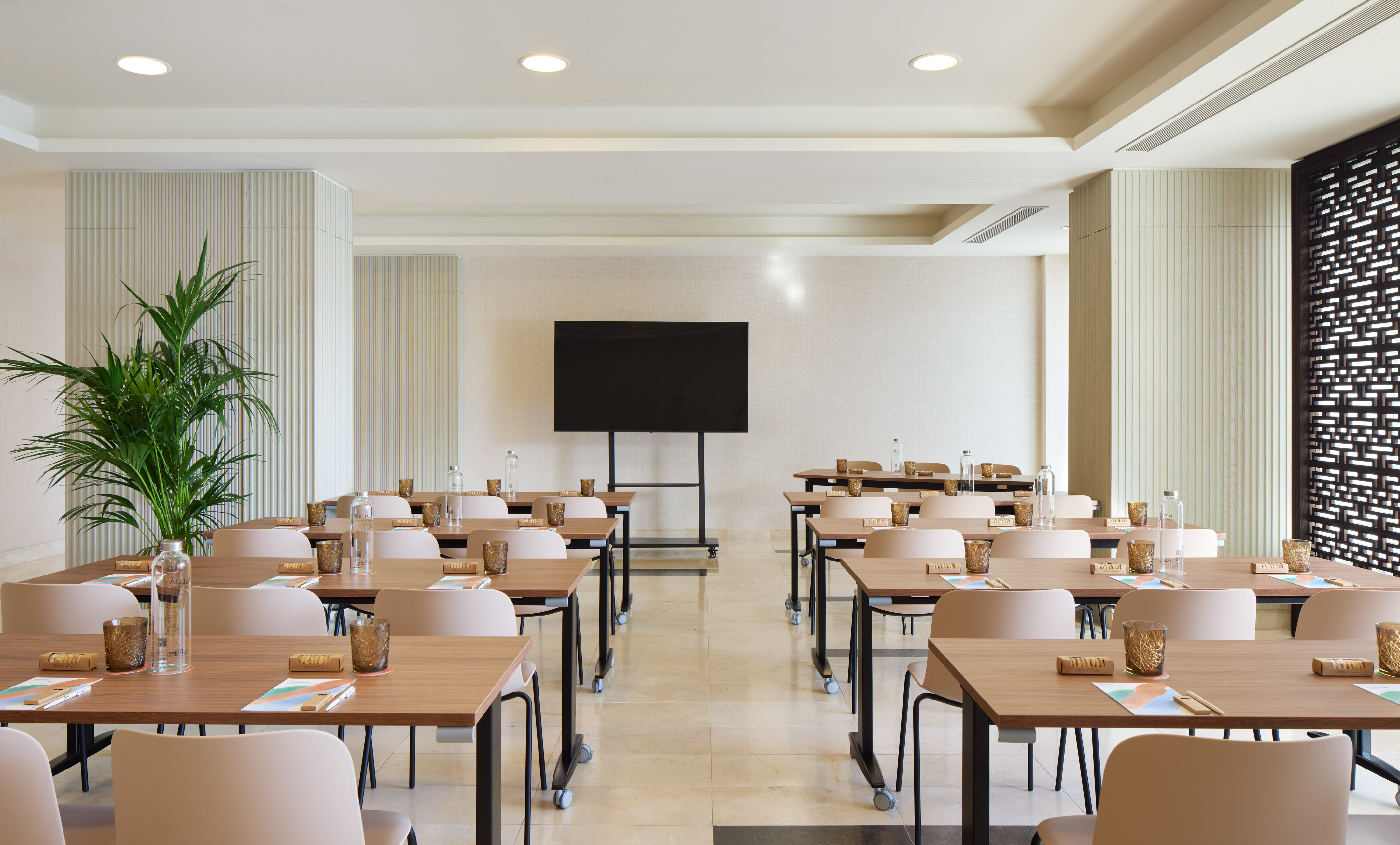 Modern training room with rows of tables, chairs, water, and large screen display.