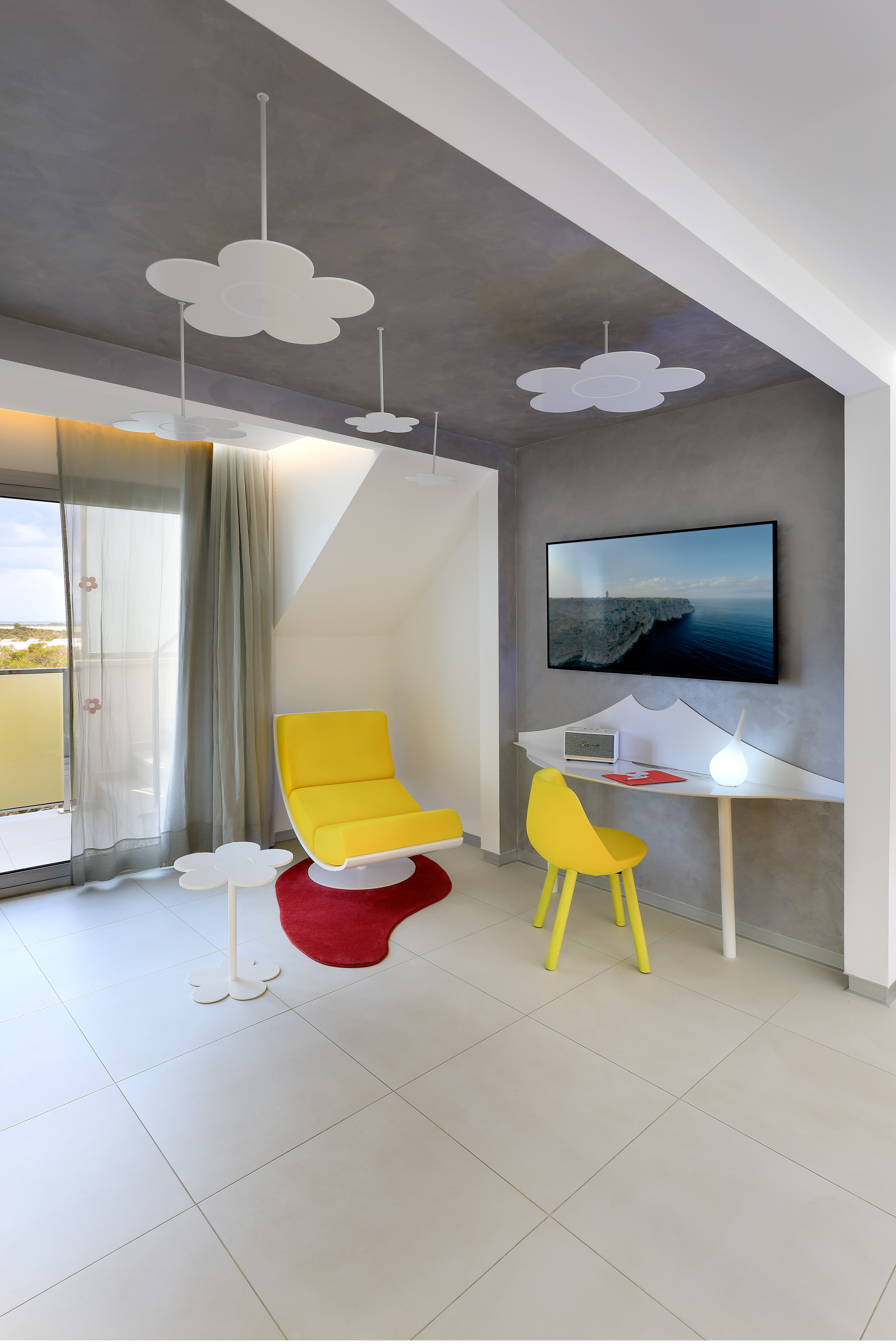 Modern room interior with yellow armchair, flower lights, TV, desk, and balcony.