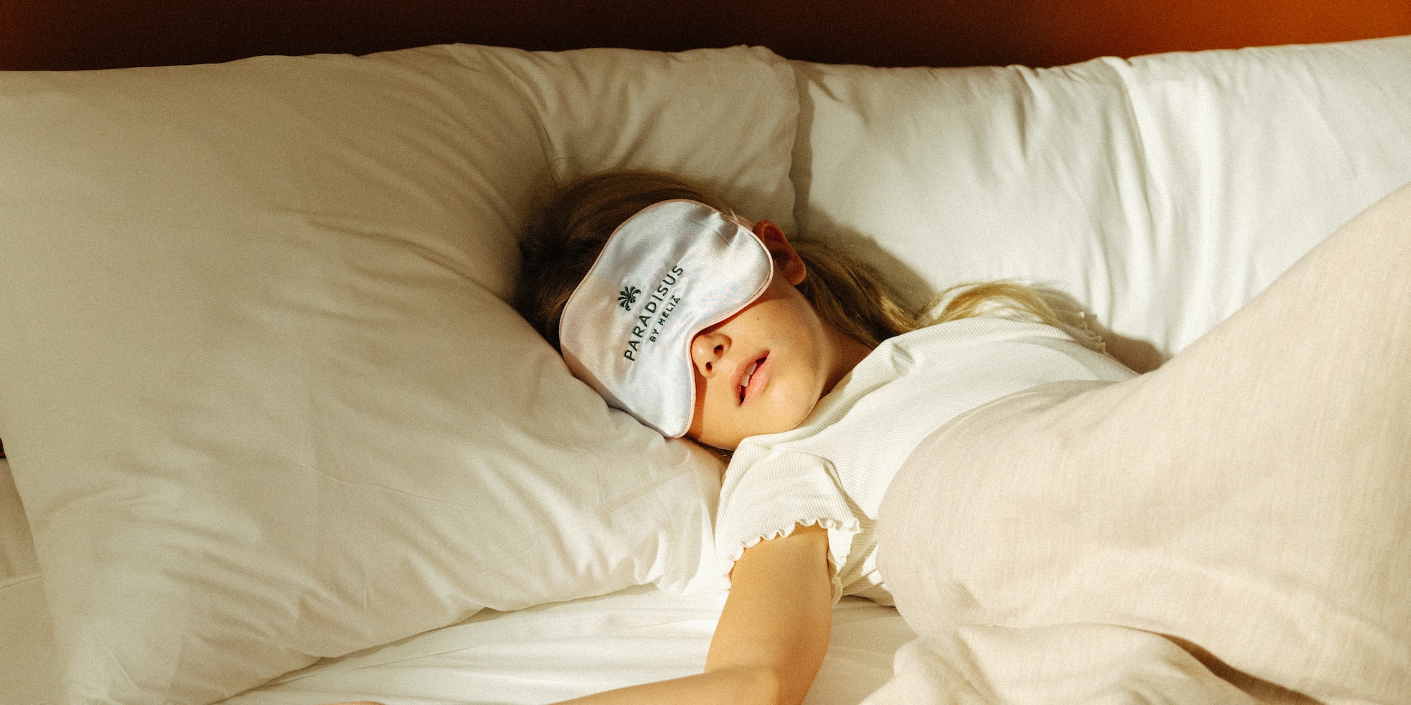 Sleeping person wearing Paradisus Meliá eye mask in cozy bed.