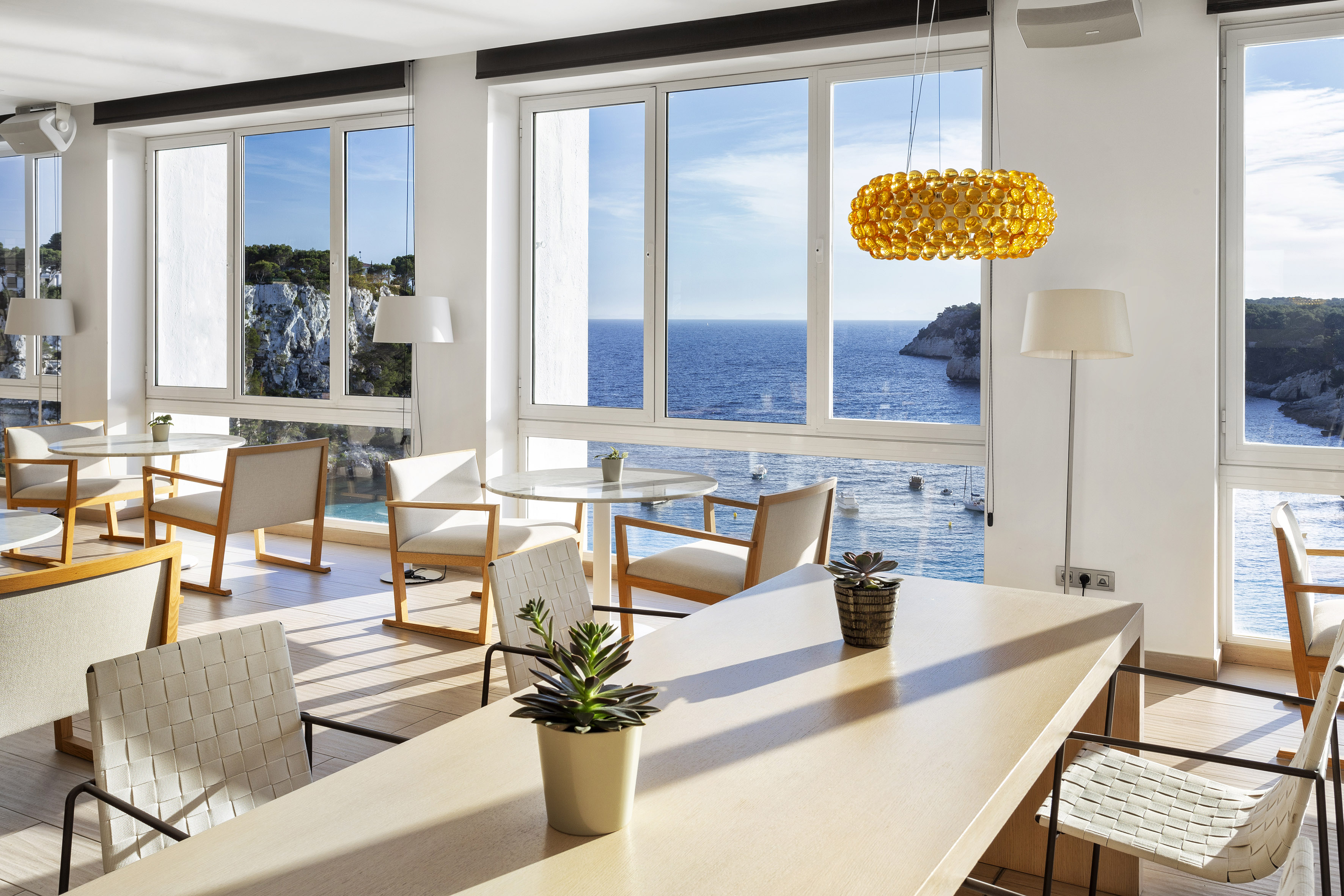 Modern coastal restaurant with large windows overlooking blue sea and cliffs.