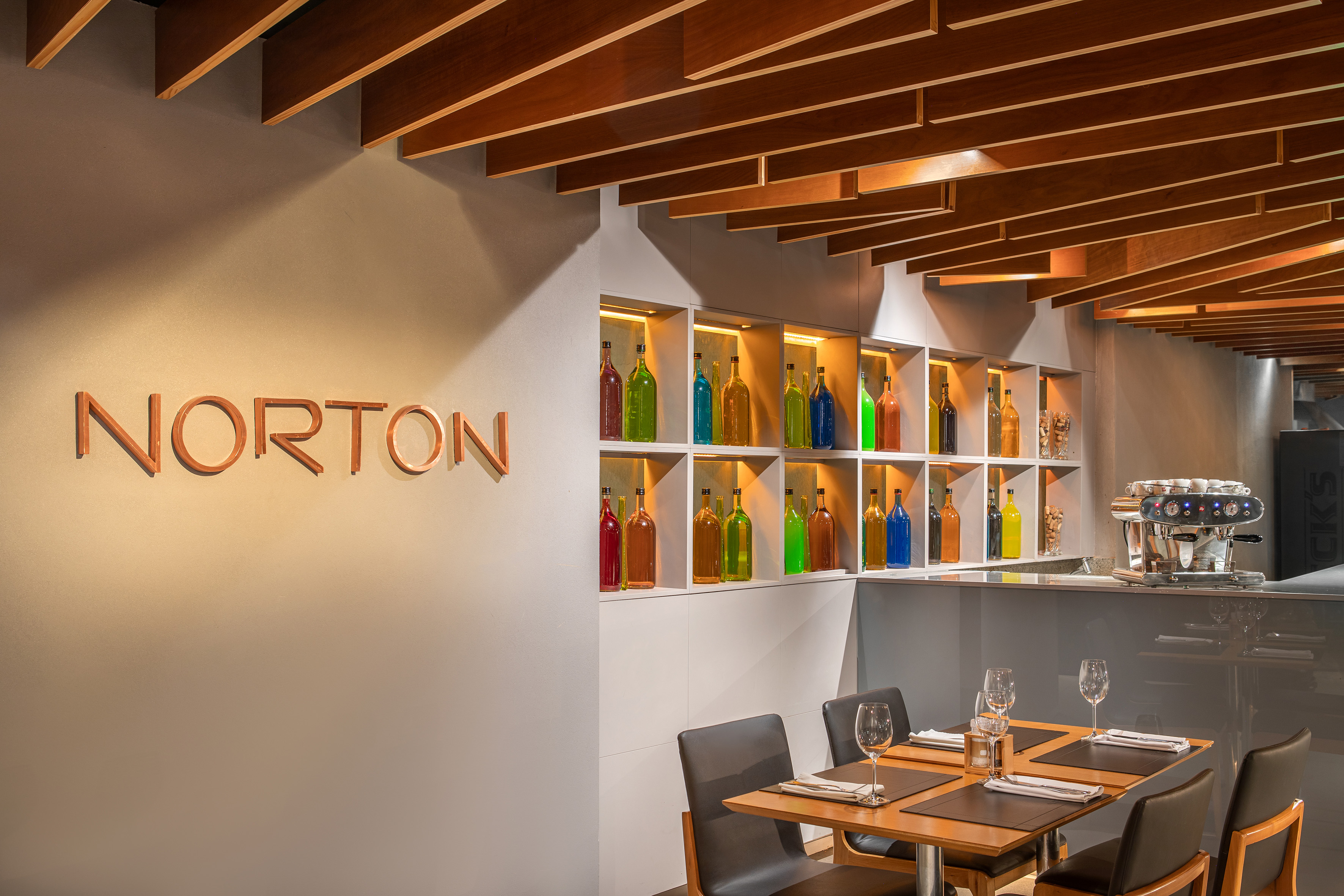 NORTON cafe interior with colorful bottles, wooden ceiling, and dining tables.