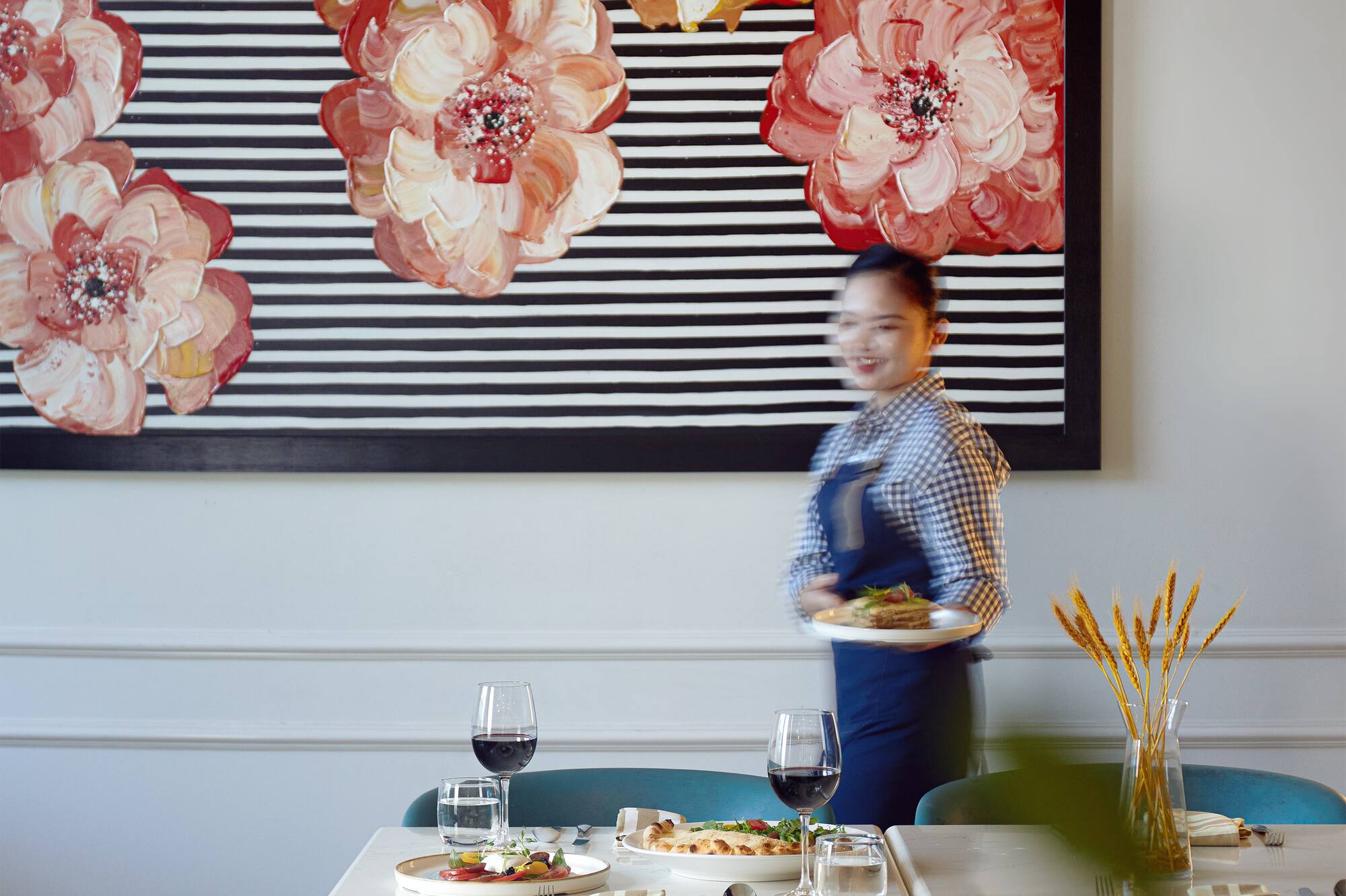 Waitress serves food in modern restaurant featuring floral stripe painting.