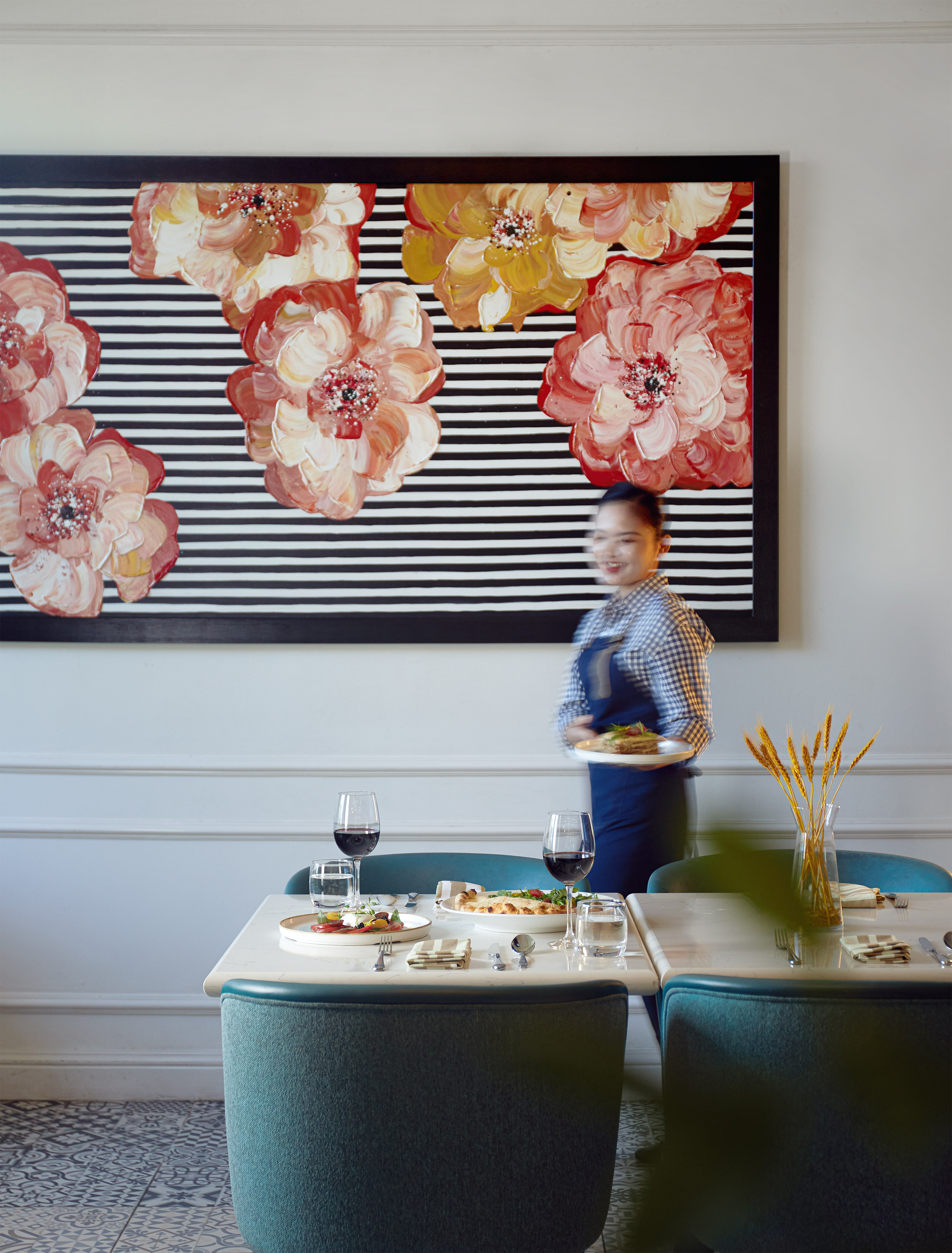 Waitress serves food in modern restaurant featuring floral stripe painting.