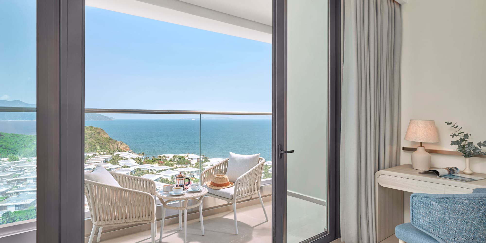 Ocean view balcony with outdoor seating, coffee, and a coastal resort landscape.