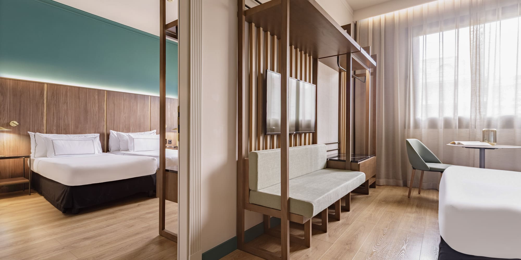 Modern hotel room with bed, living space, wood partition, and large window.