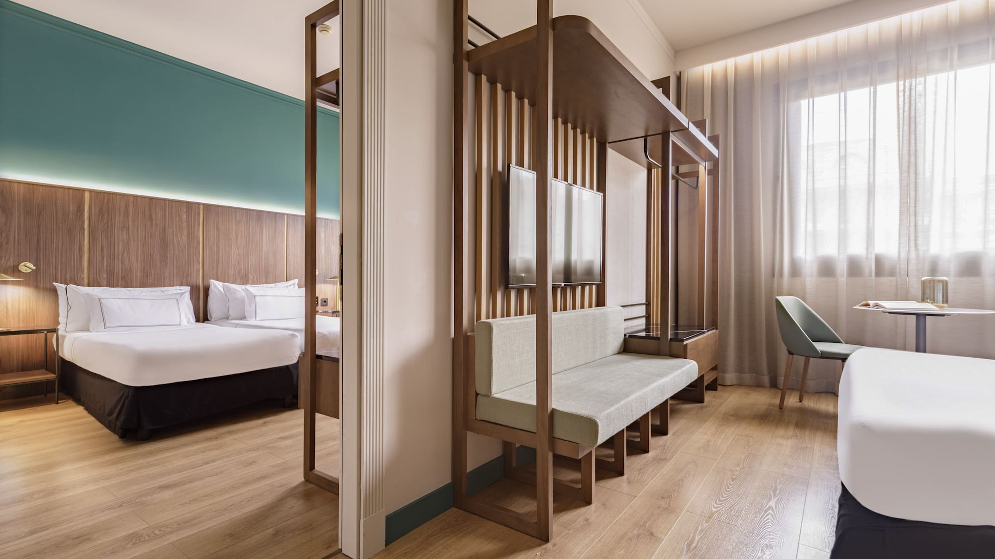 Modern hotel room with bed, living space, wood partition, and large window.