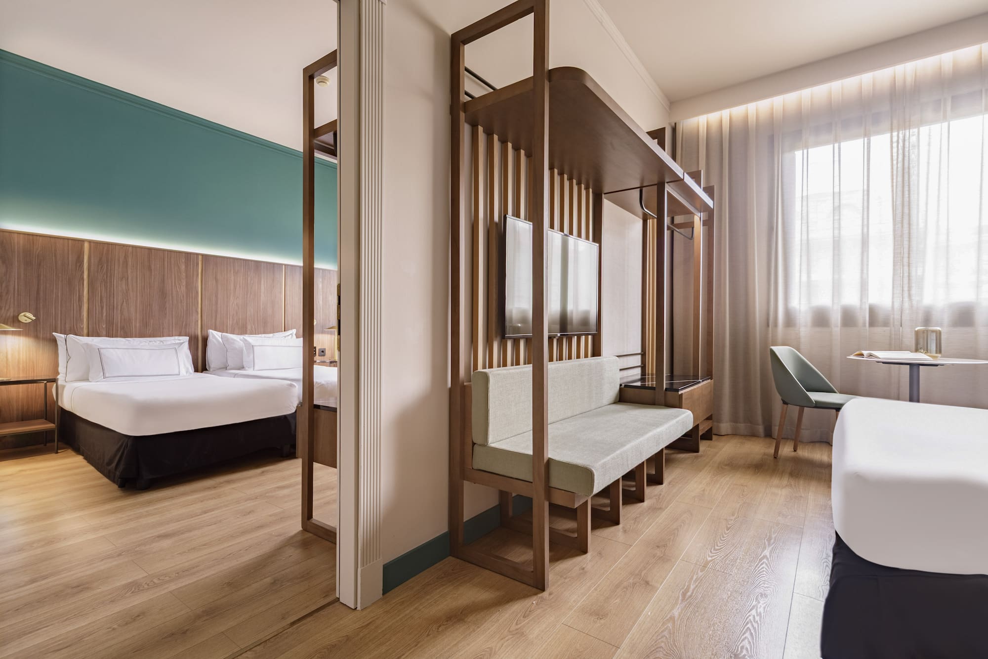 Modern hotel room with bed, living space, wood partition, and large window.