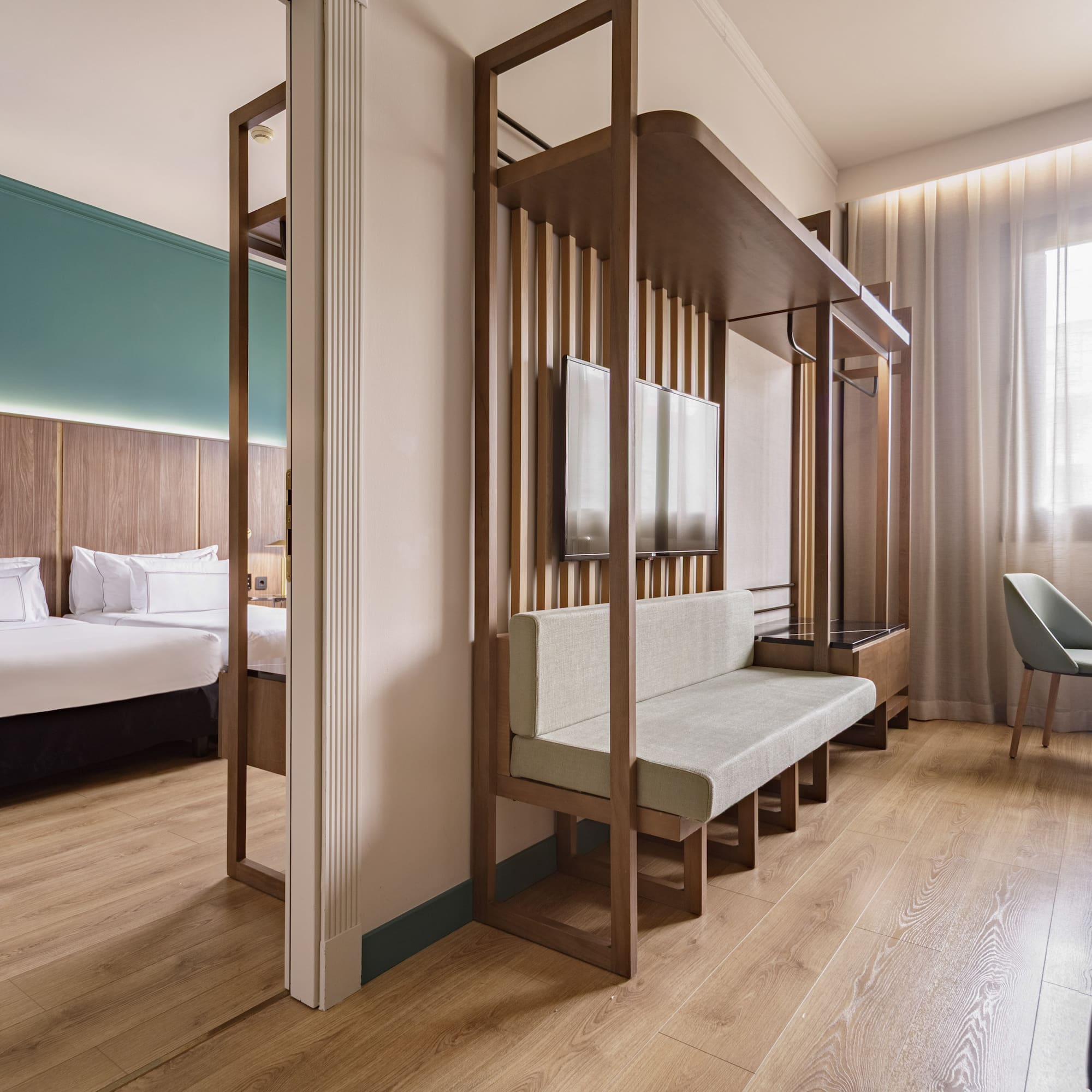 Modern hotel room with bed, living space, wood partition, and large window.