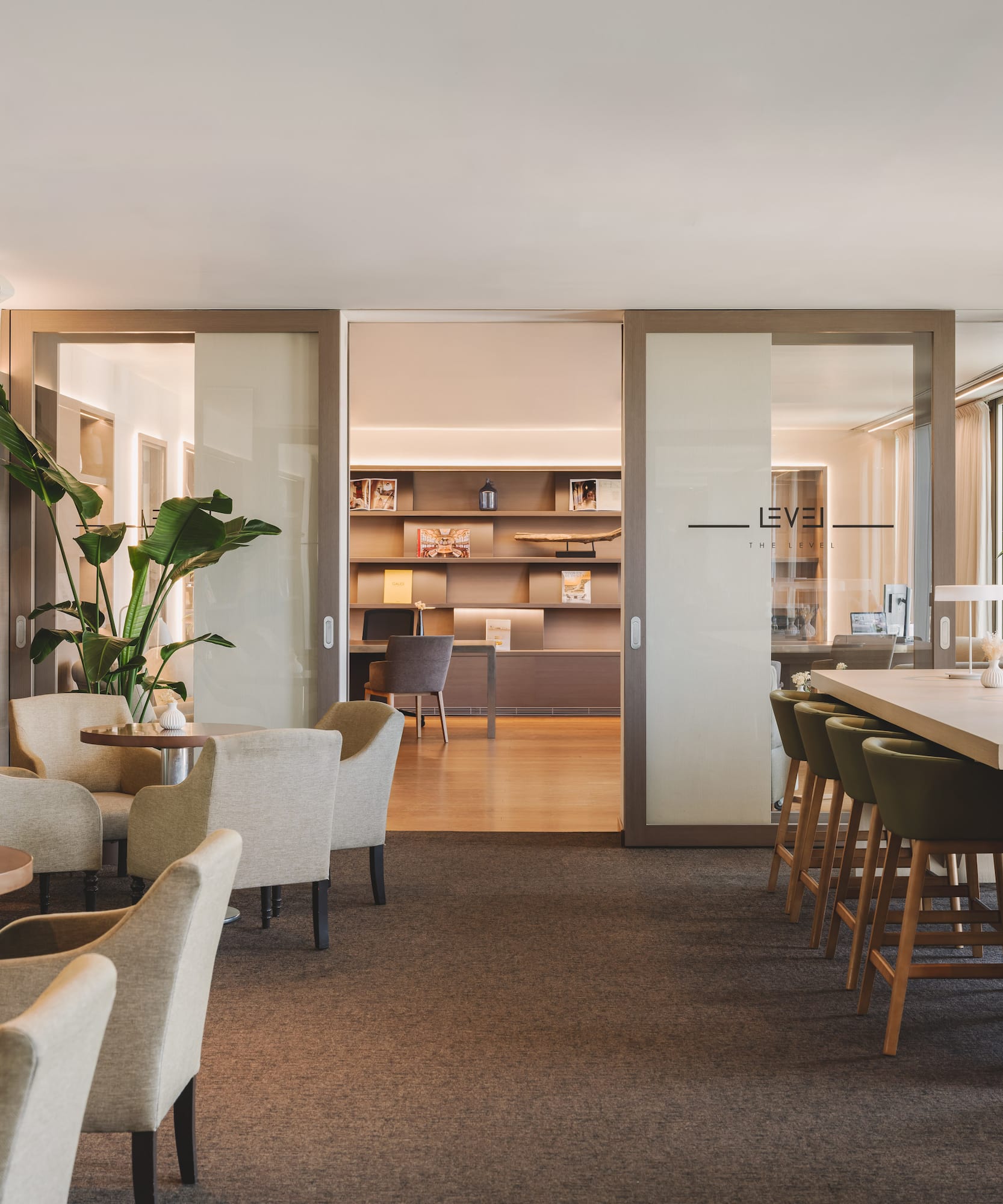 Modern executive lounge with armchairs, long communal table, and bookshelves.