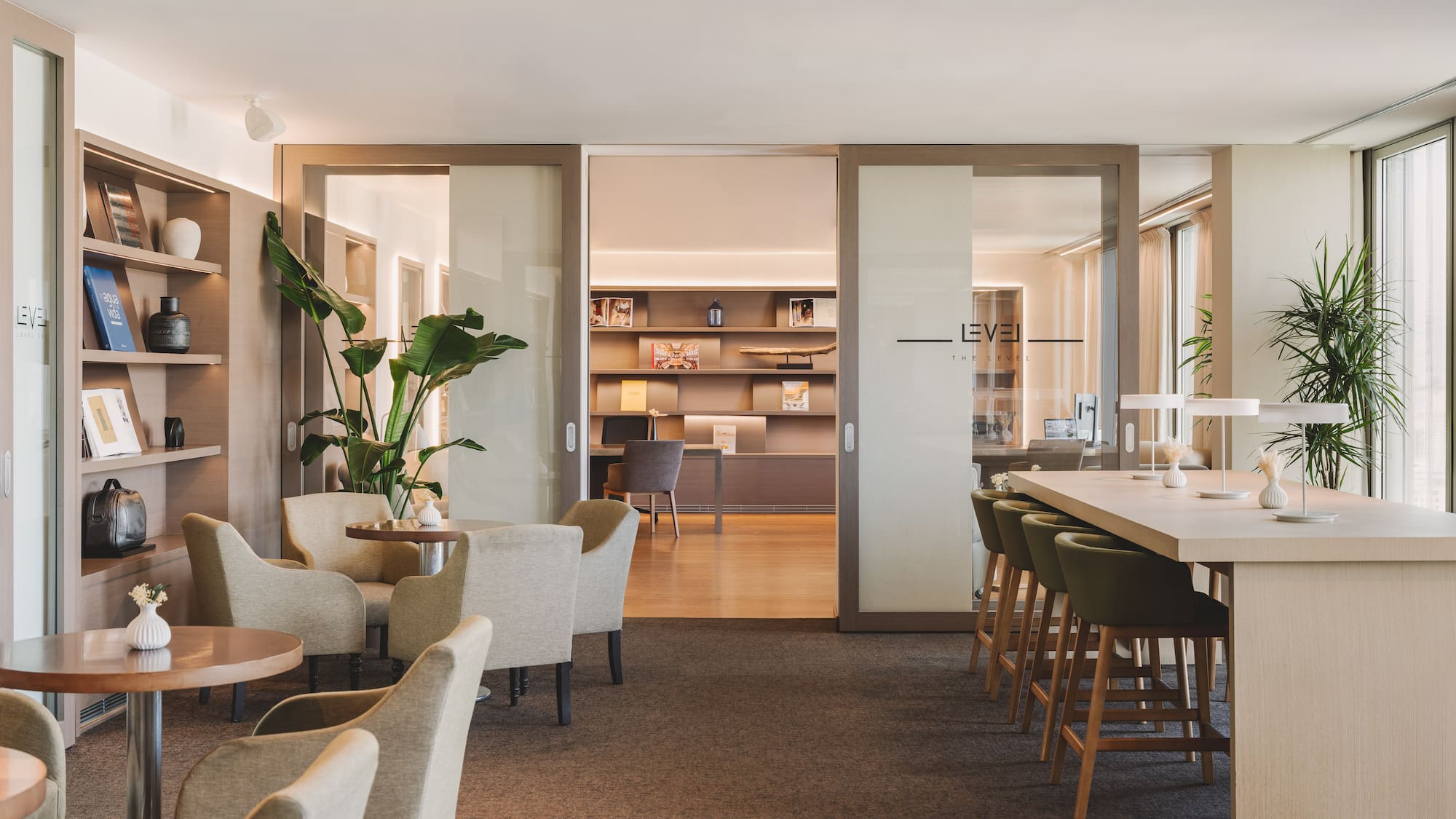 Modern "LEVEL" lounge with diverse seating, bookshelves, and lush plants.