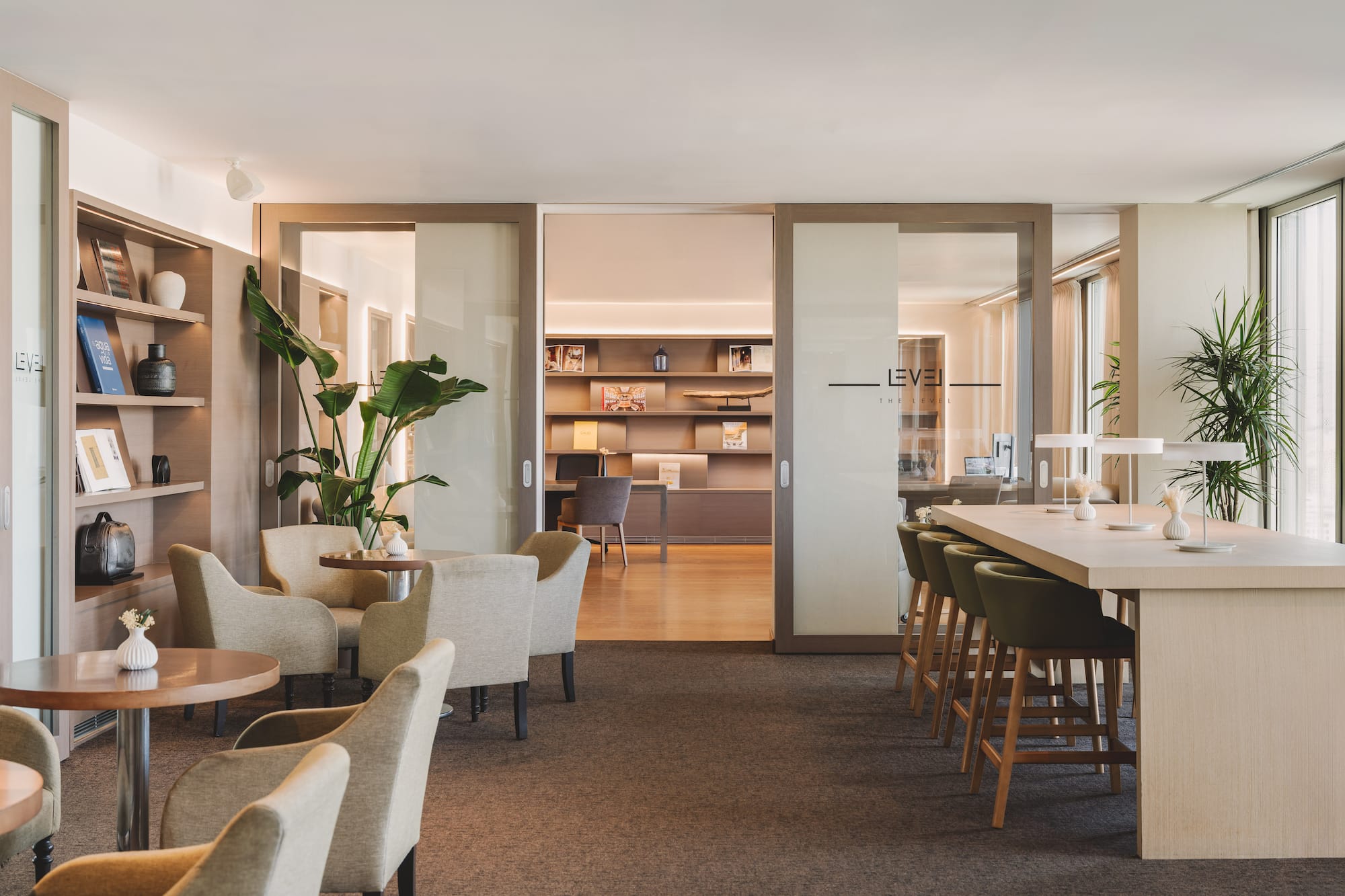 Modern executive lounge with armchairs, long communal table, and bookshelves.