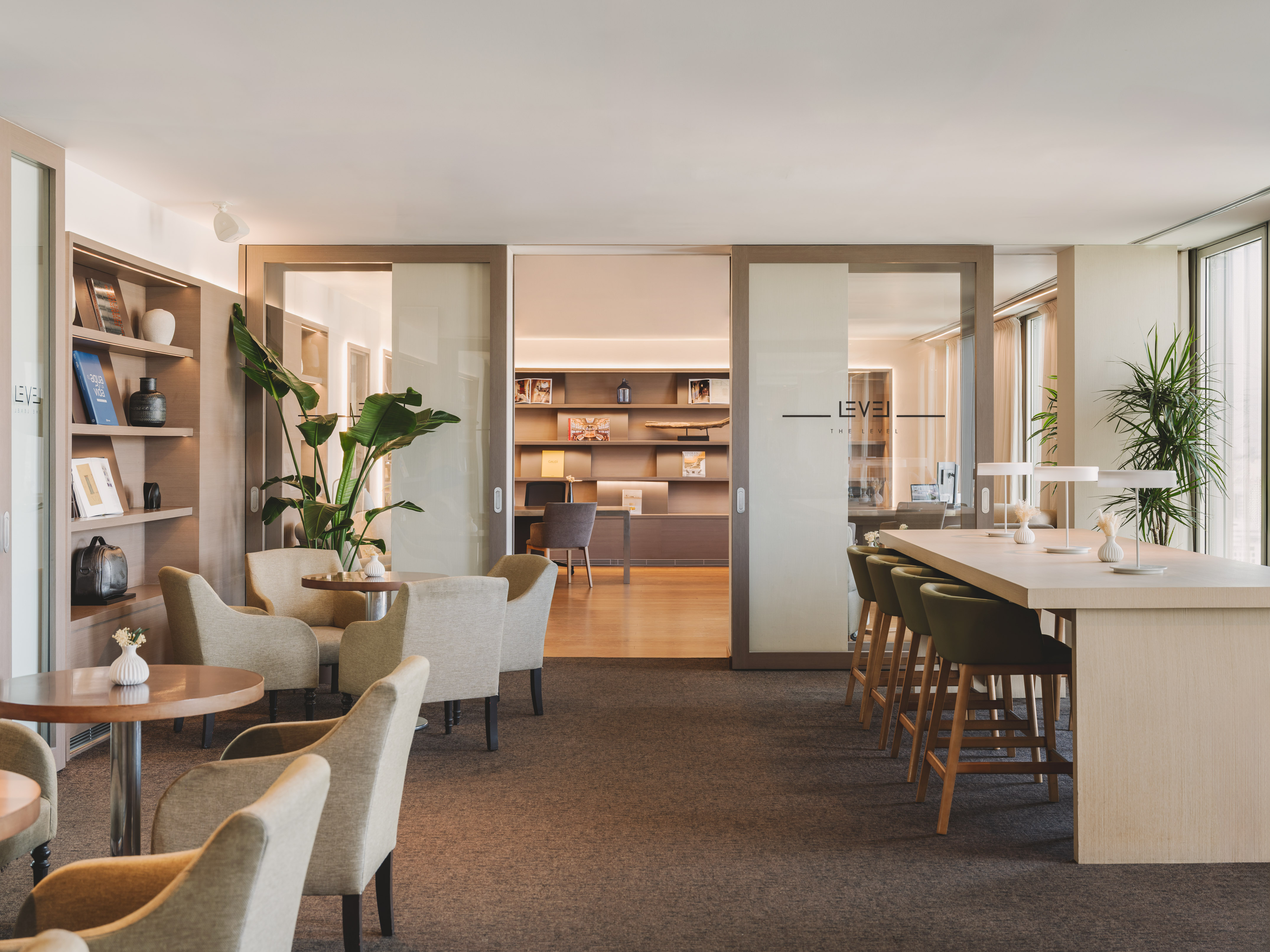 Espacio lounge moderno con sillones, barra alta y estantes en hotel.