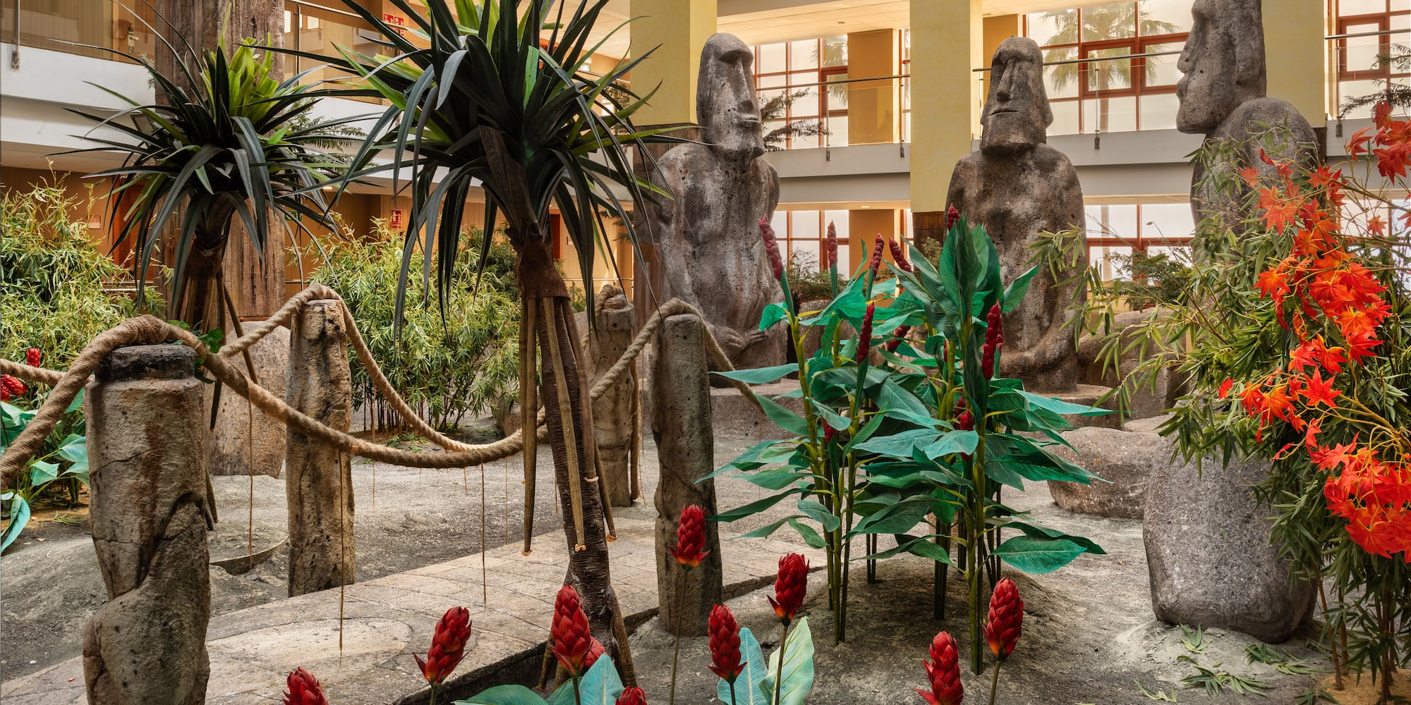 Tropical indoor garden with Moai statues and red ginger flowers.
