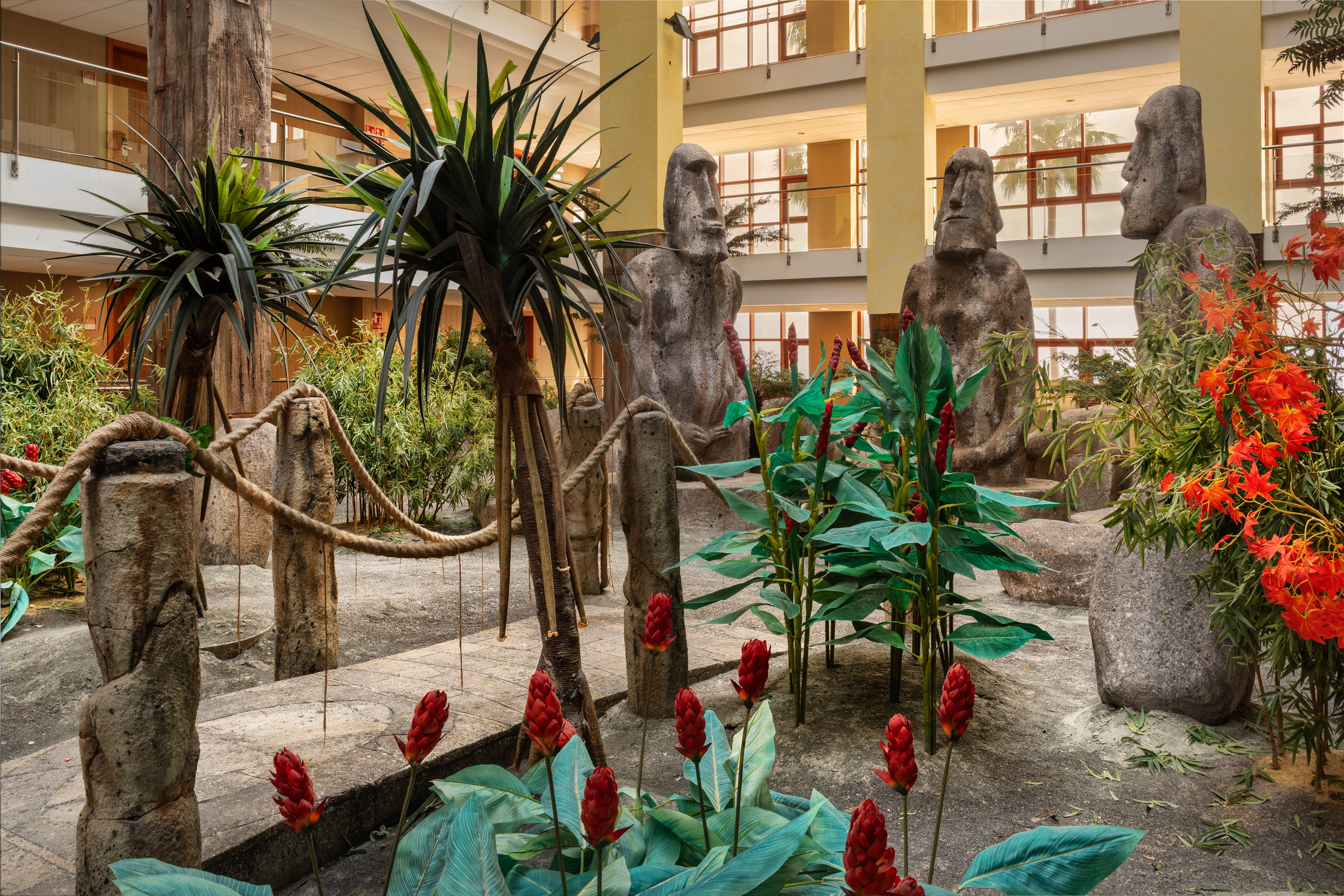 Tropical indoor garden with Moai statues and red ginger flowers.