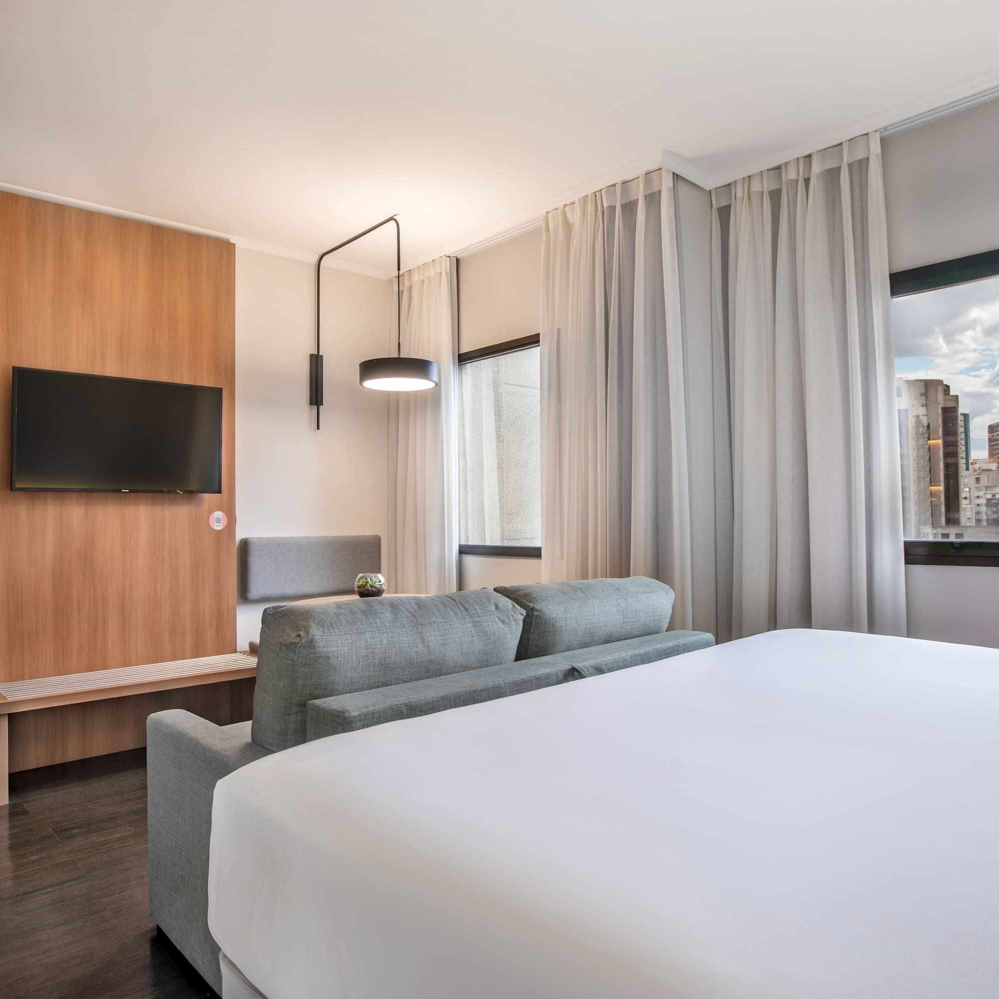 Habitación moderna de hotel: cama, sofá, TV, vista ciudad, colchoneta yoga.