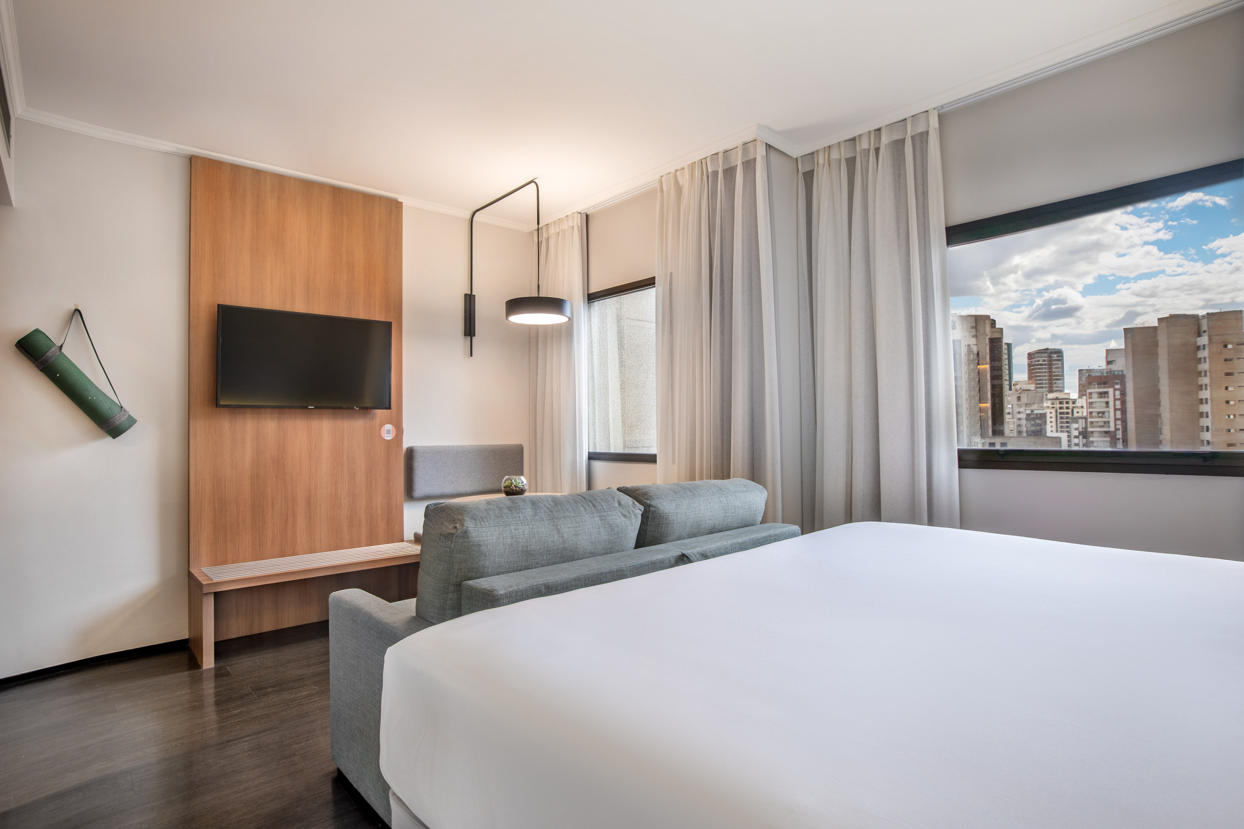 Habitación moderna de hotel: cama, sofá, TV, vista ciudad, colchoneta yoga.