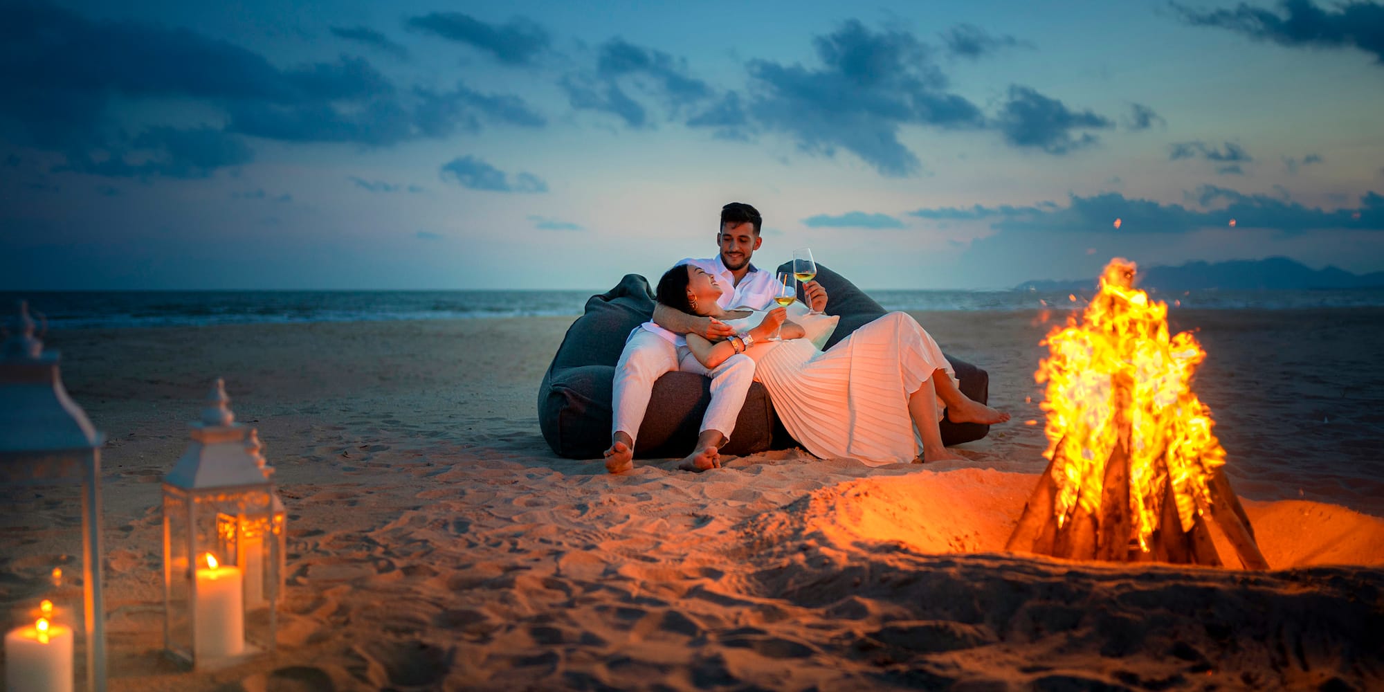 a man and woman sitting on a bean bag chair on a beach