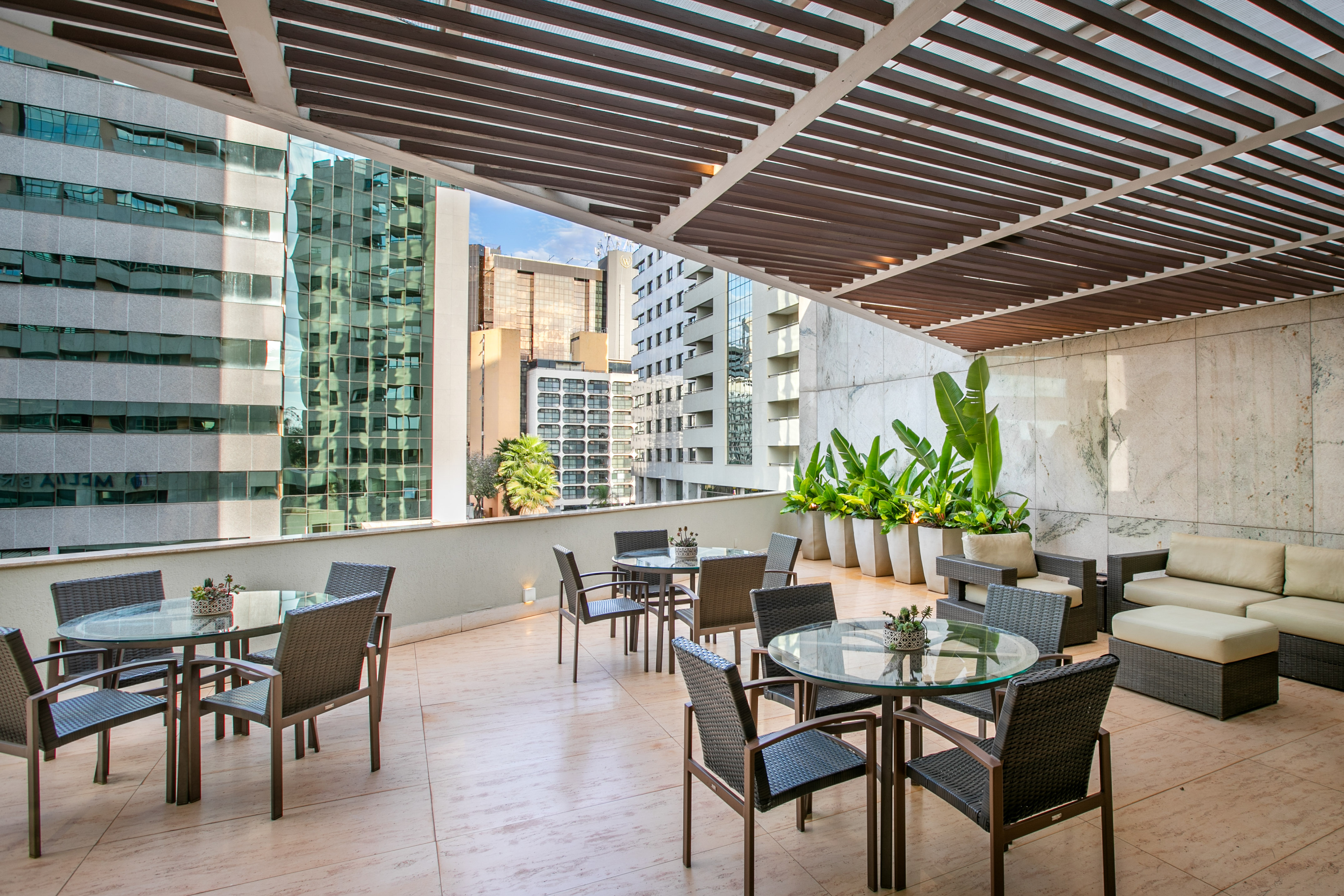 Modern outdoor terrace with dining tables, lounge, green plants, and city skyline.