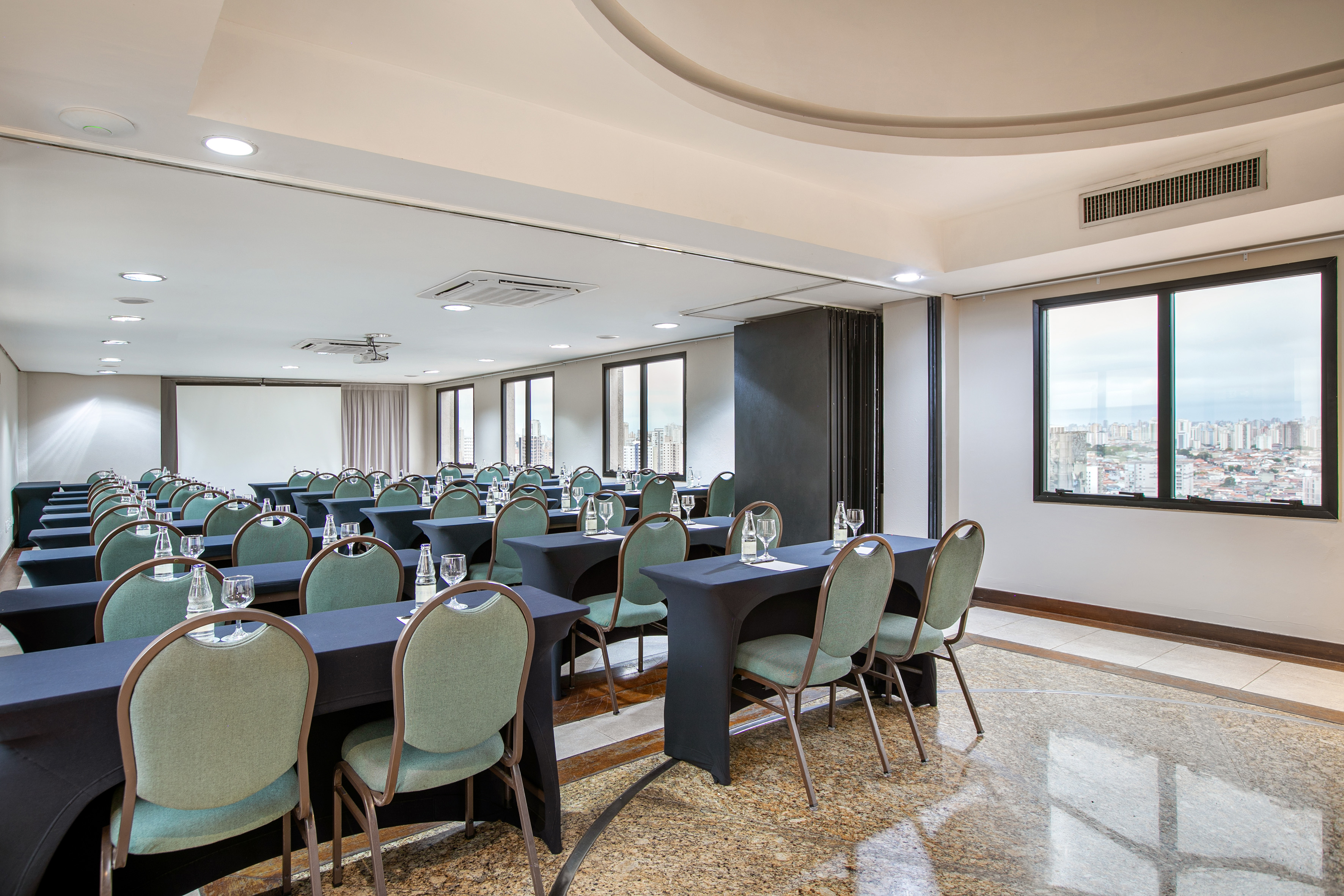 Conference room setup with green chairs, draped tables, projector, city view.