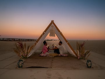 a man and woman sitting on a mat under a tent on a beach