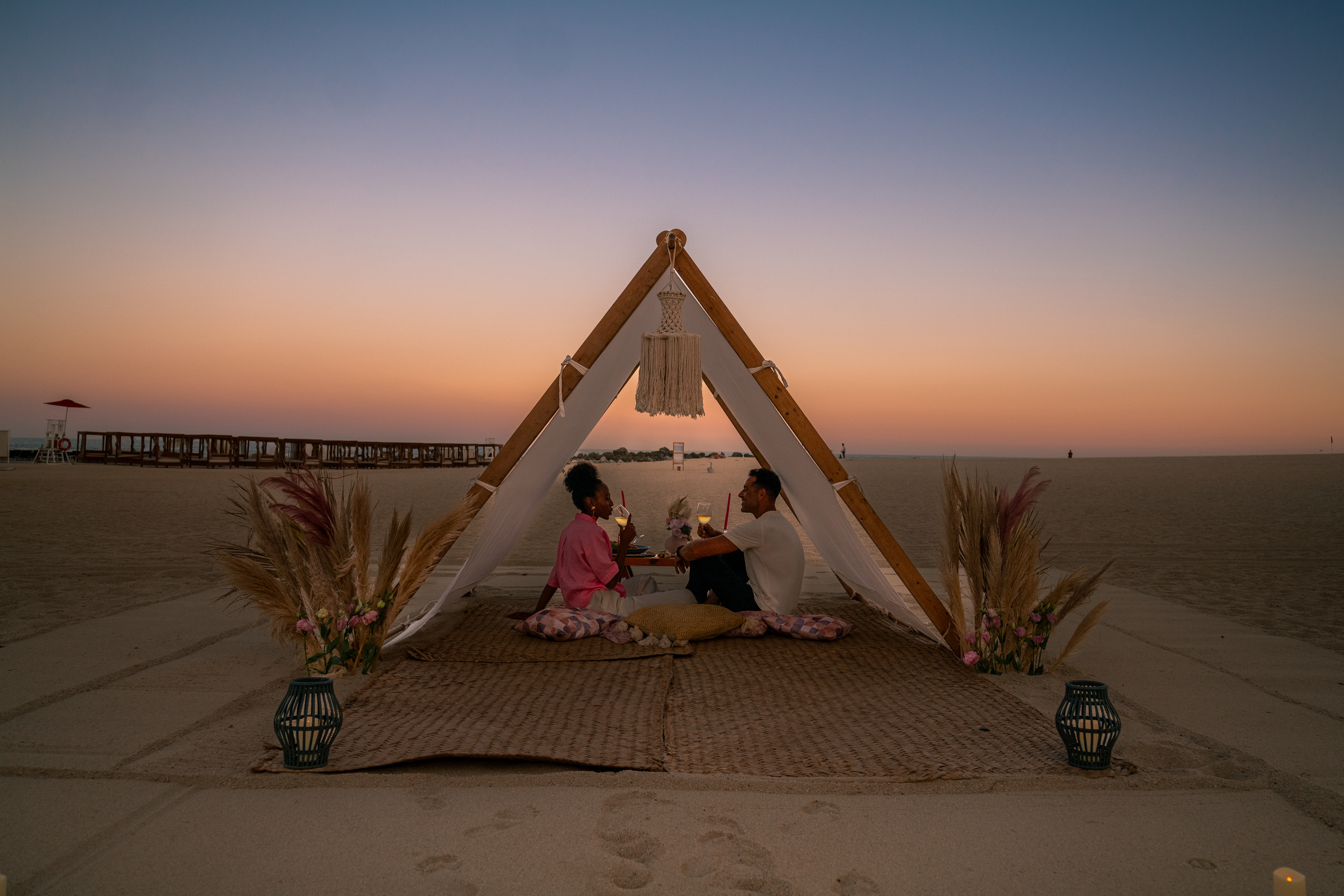 a man and woman sitting on a mat under a tent on a beach