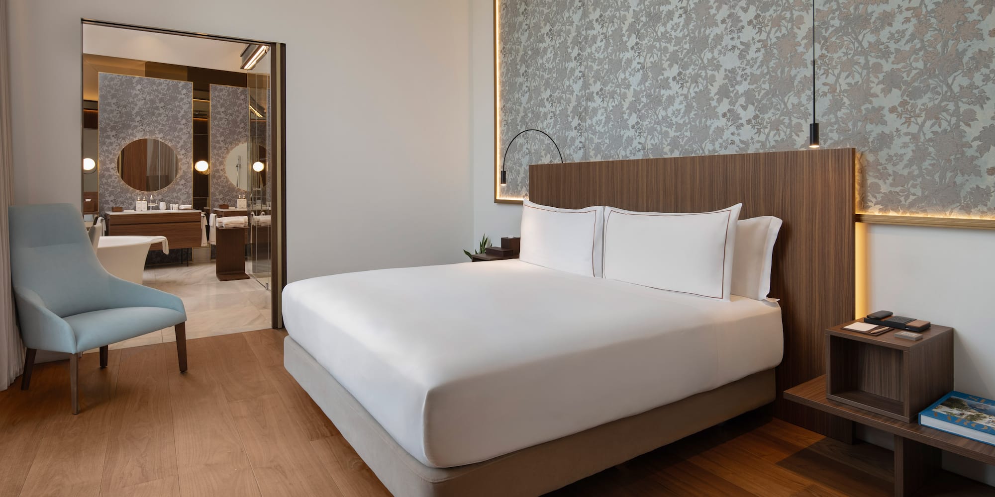Modern luxury hotel bedroom with large bed, wood floor, and en-suite bathroom.