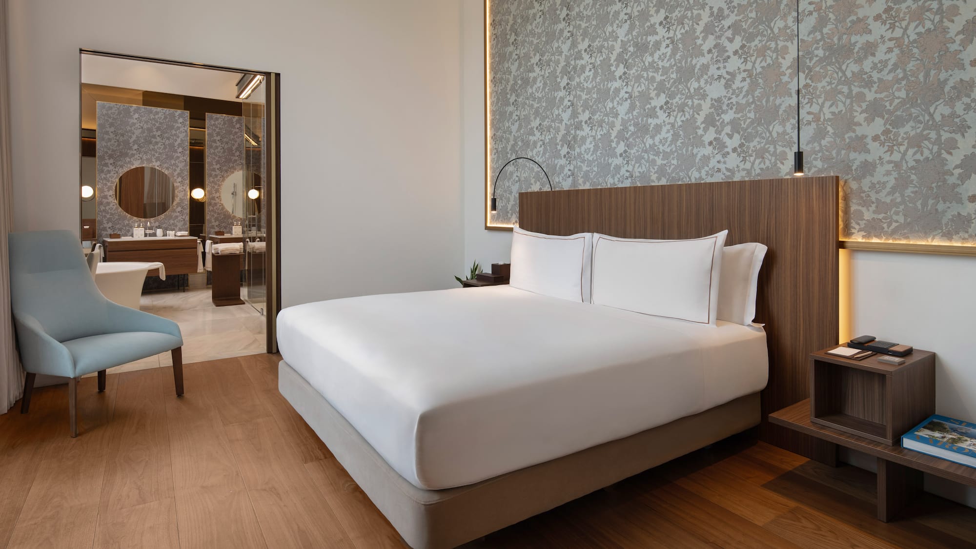 Modern luxury hotel bedroom with large bed, wood floor, and en-suite bathroom.