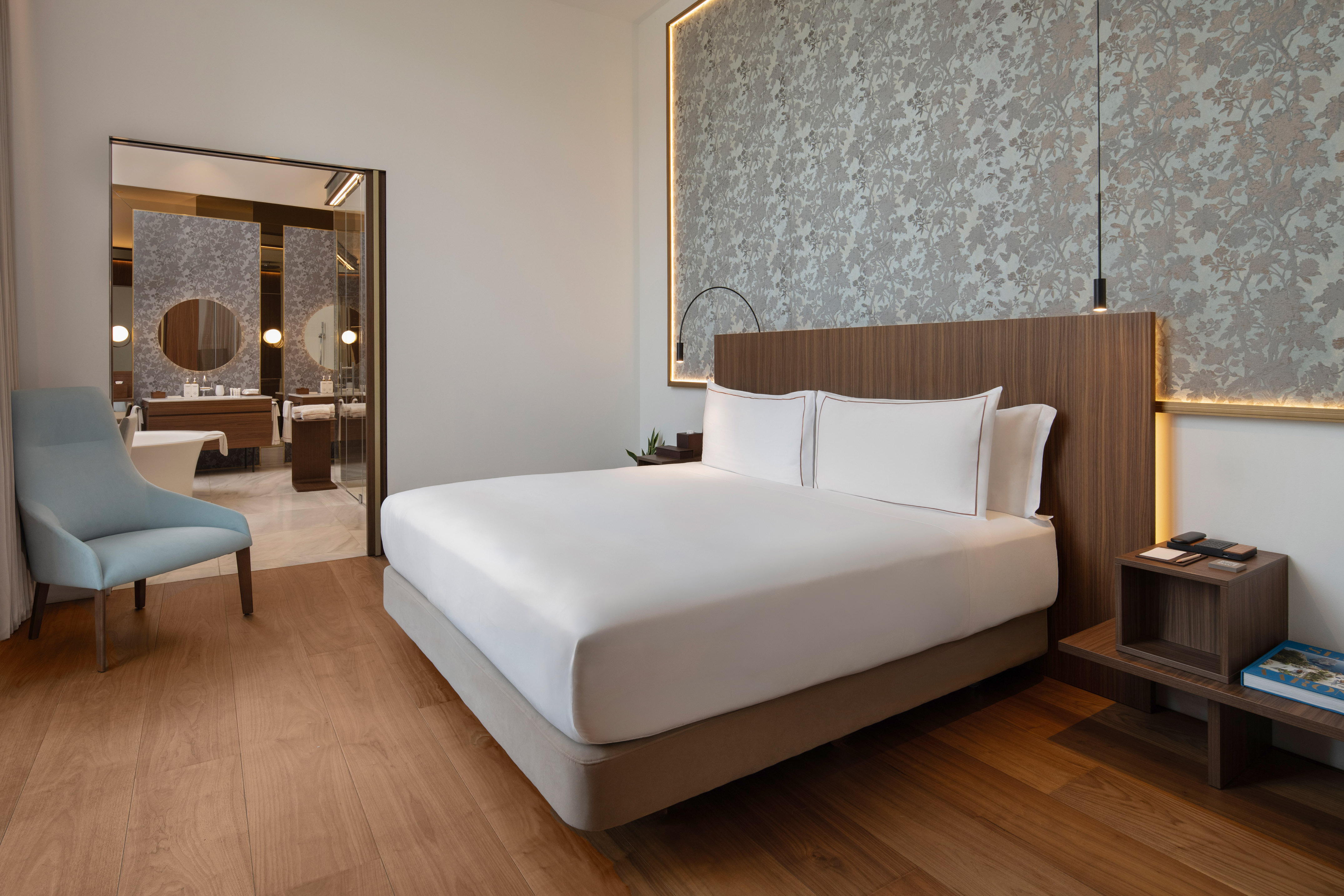 Modern luxury hotel bedroom with large bed, wood floor, and en-suite bathroom.