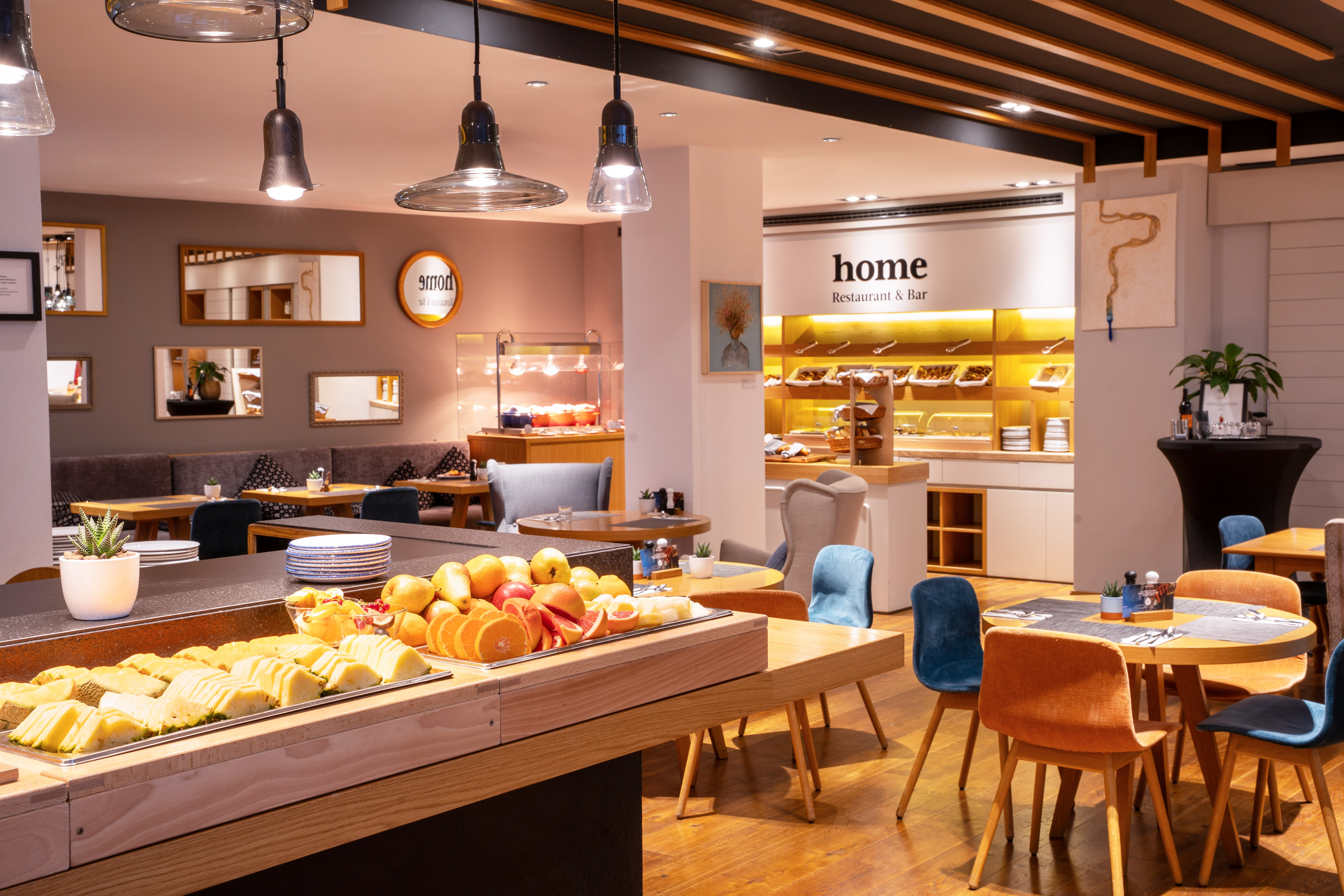 Hotel restaurant with fresh fruit breakfast buffet and 'Home' sign.