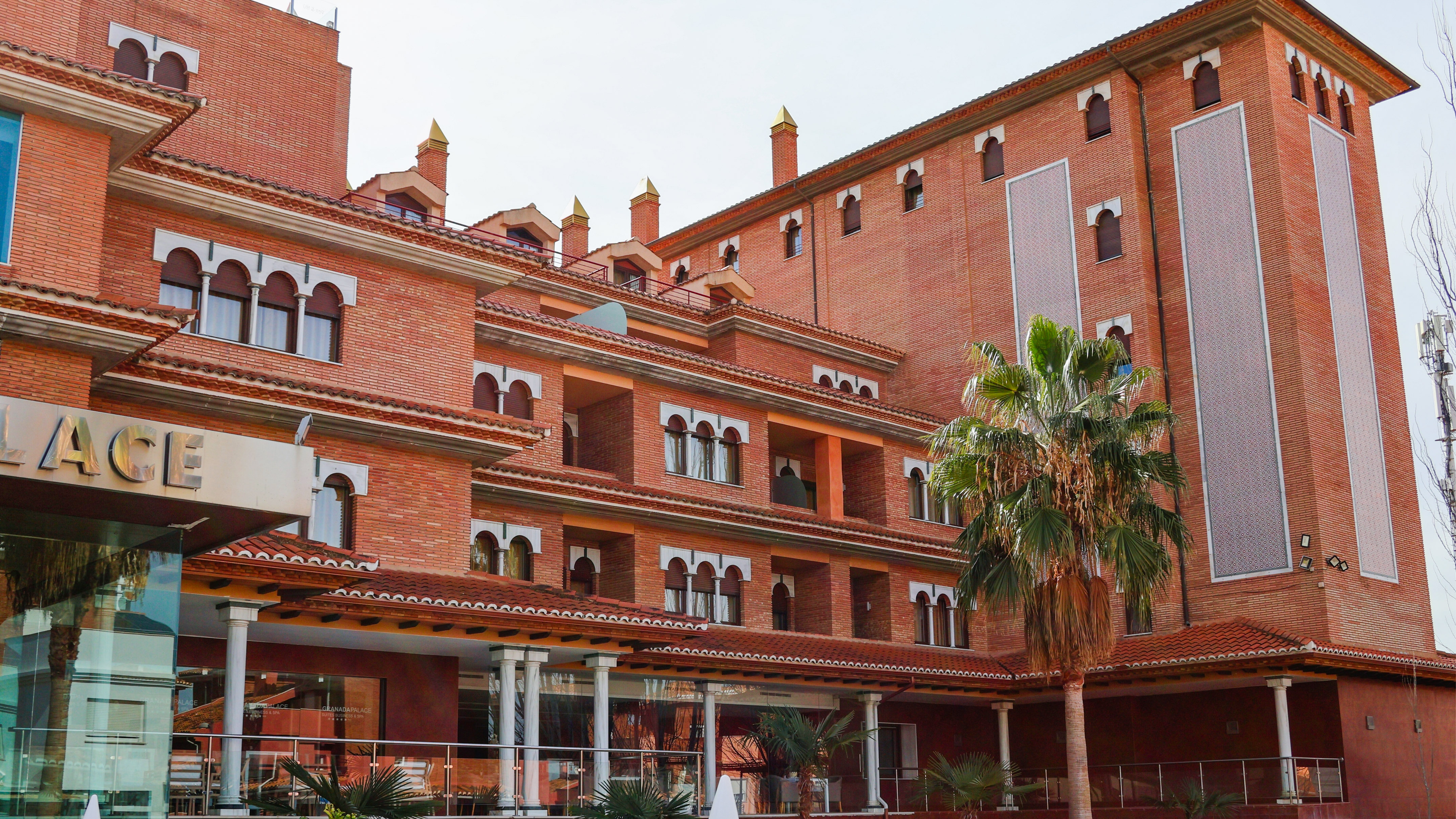 Andalusian-style brick hotel with arched windows and a prominent palm tree.