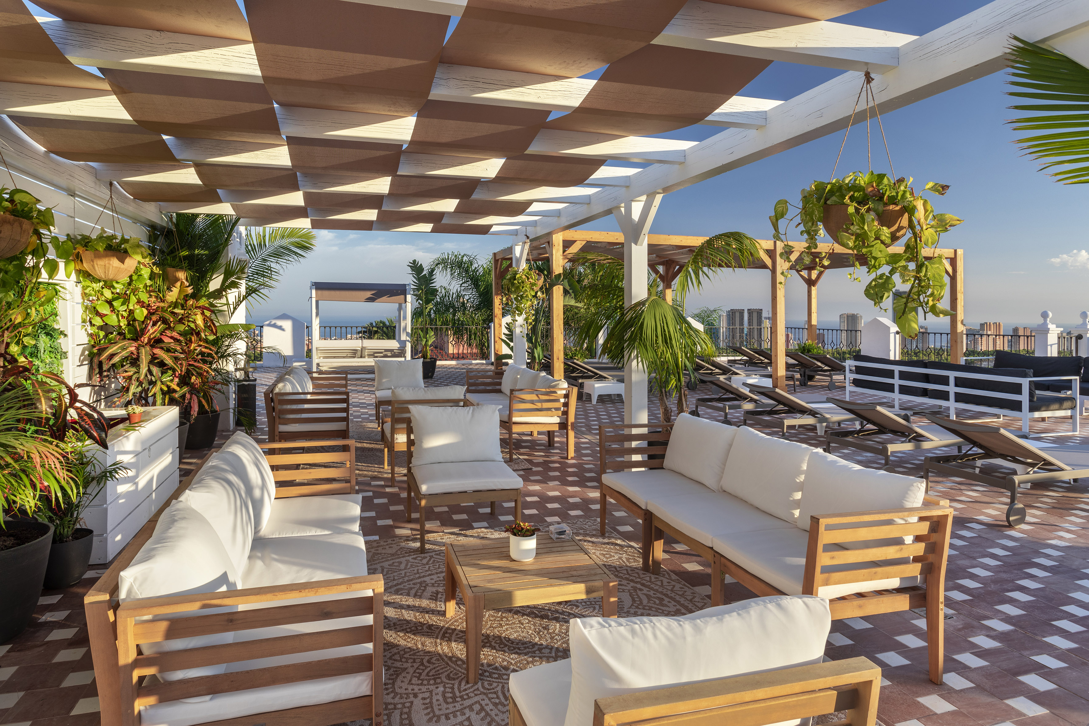 Sunny rooftop terrace with pergola shade, outdoor lounge furniture, and lush plants.