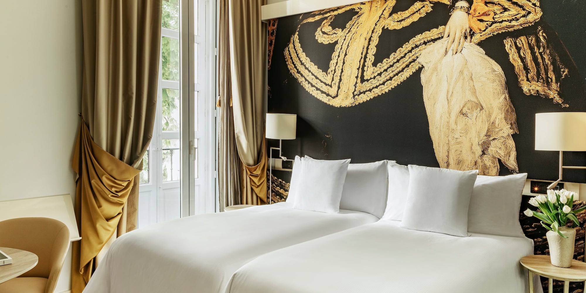 a bed with white sheets and a gold wall with a painting on the wall