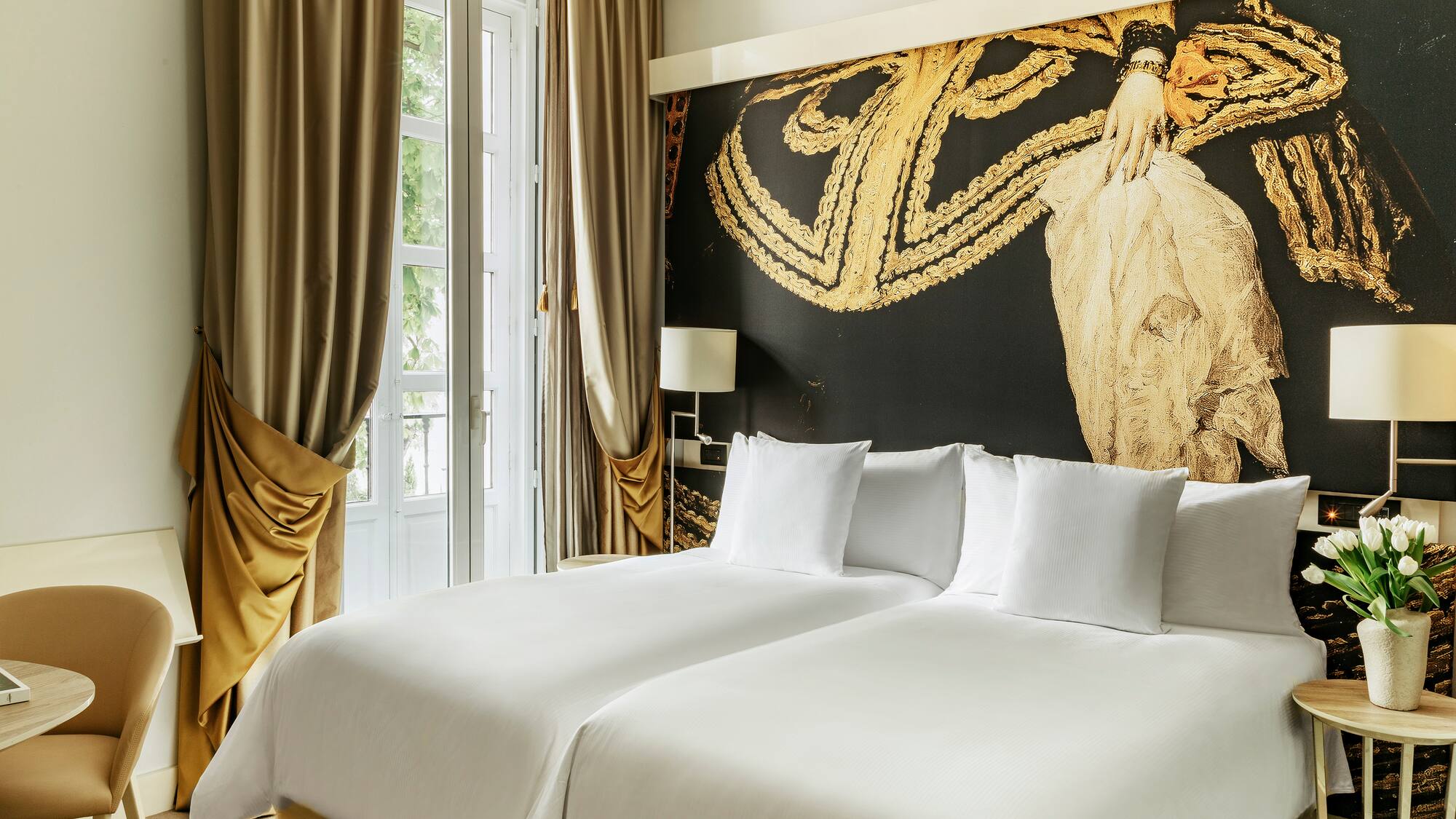 a bed with white sheets and a gold wall with a painting on the wall