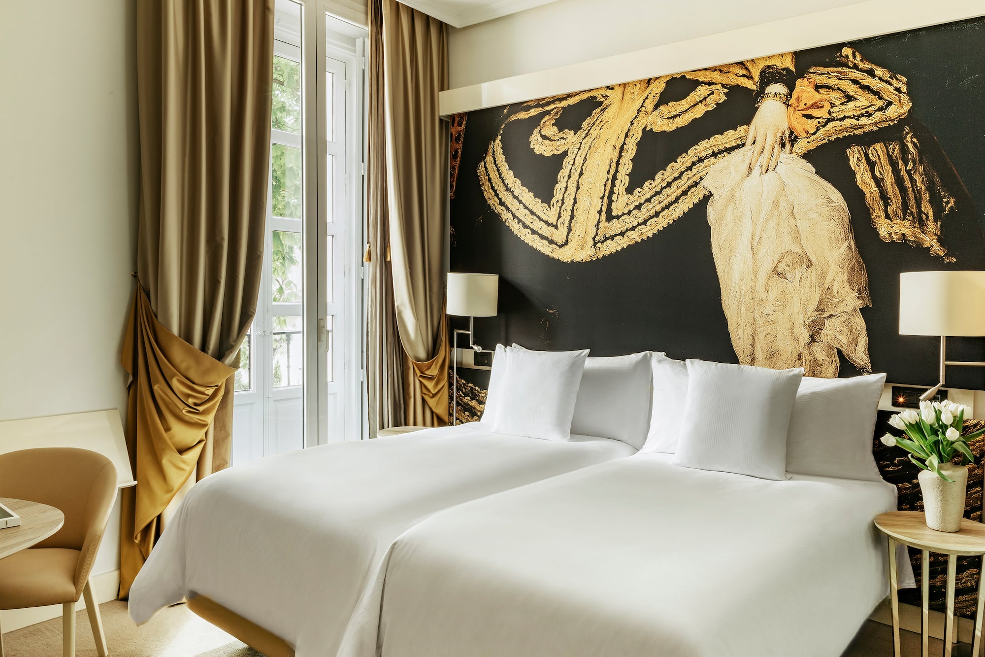 a bed with white sheets and a gold wall with a painting on the wall