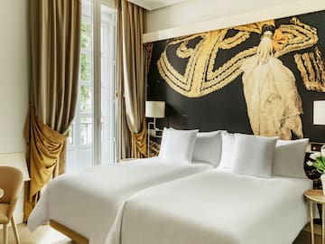 a bed with white sheets and a gold wall with a painting on the wall