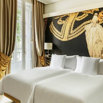 a bed with white sheets and a gold wall with a painting on the wall