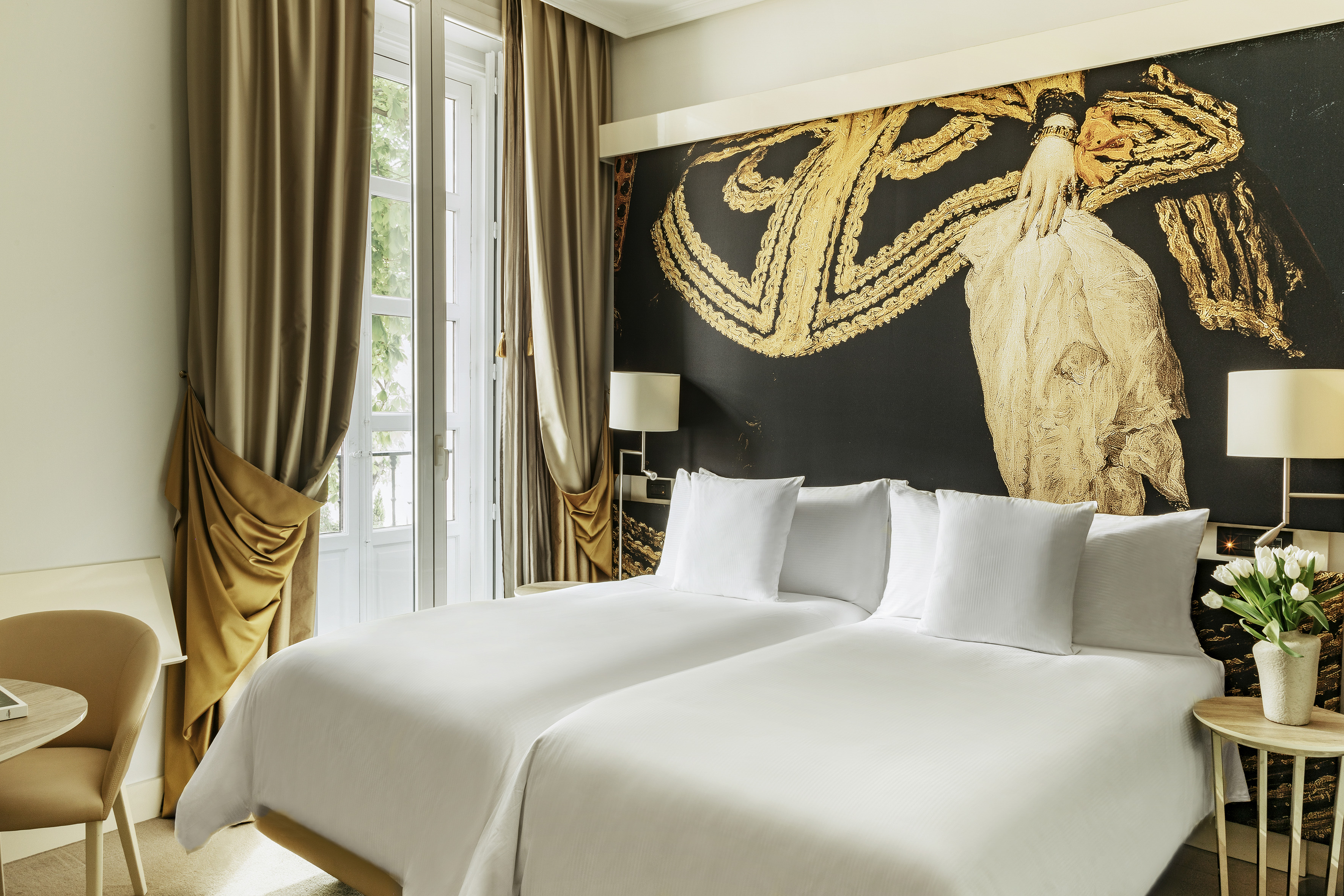 Modern hotel room with twin beds, gold mural, and balcony.