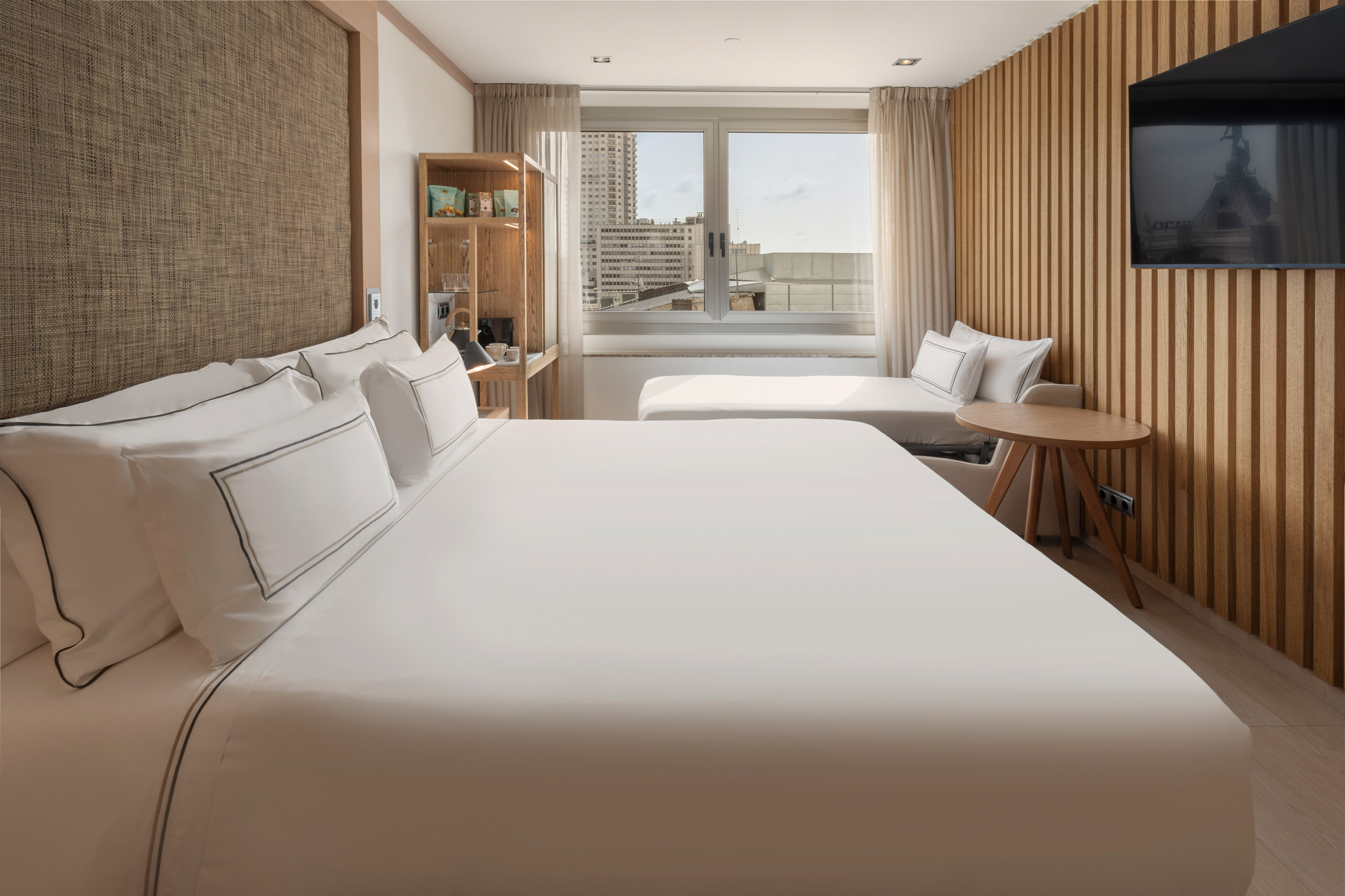 Modern hotel room with bed, city view, daybed, and wood paneling.