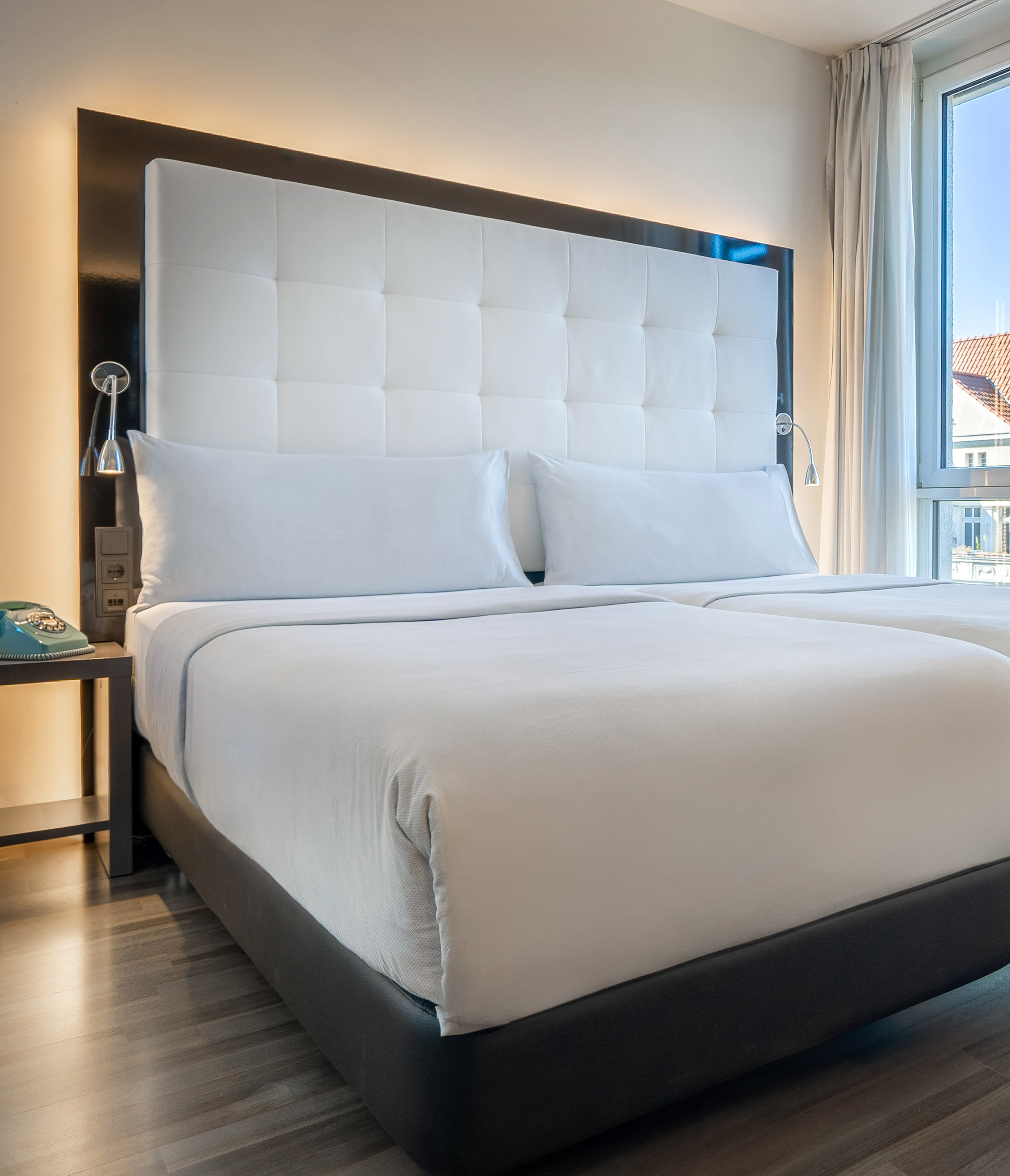Clean hotel bedroom featuring twin beds, white padded headboard, and window.