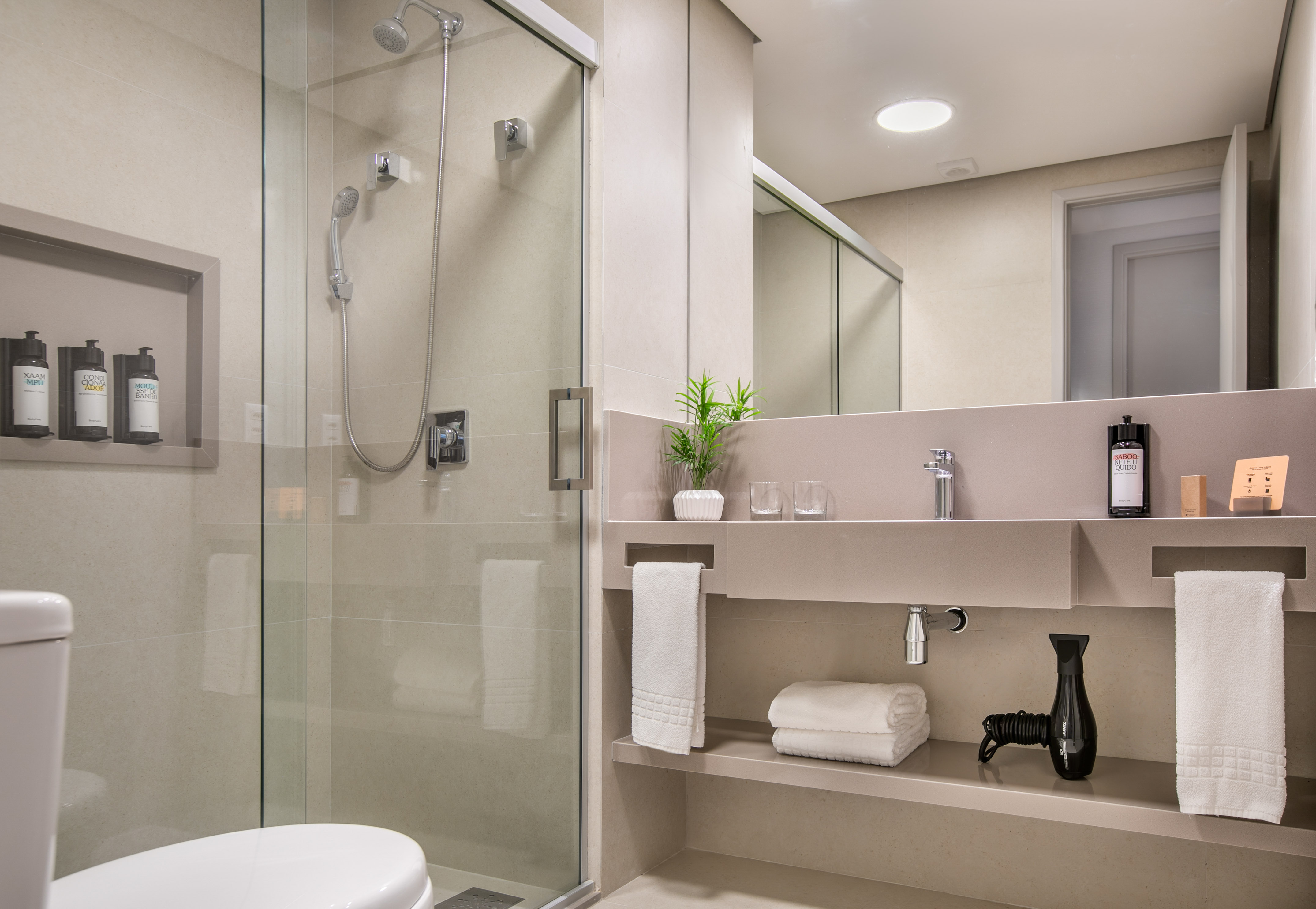 Modern hotel bathroom with glass shower, toilet, vanity, and toiletries.