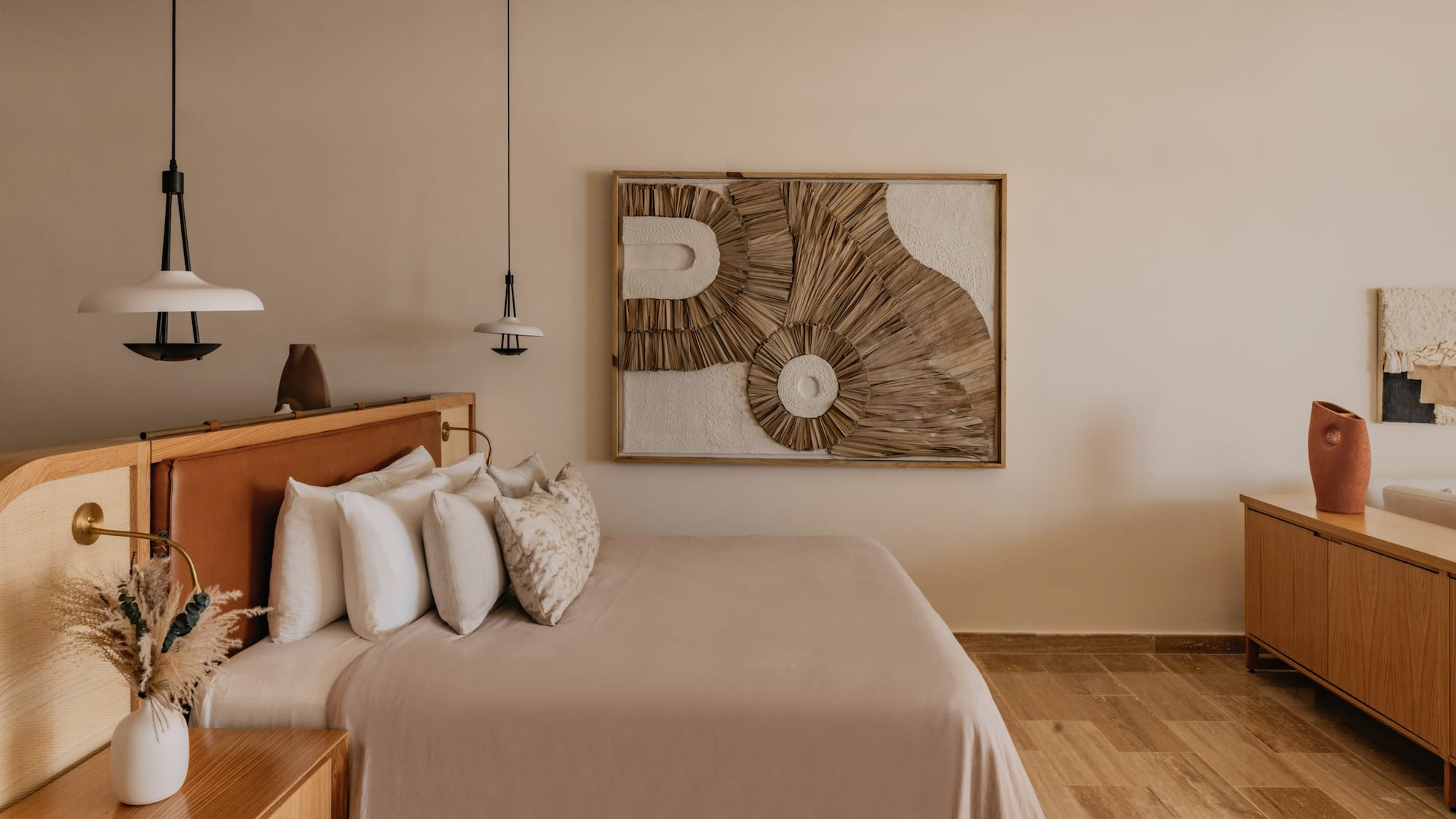 Modern boho bedroom with woven wall art, leather headboard, wood furniture.