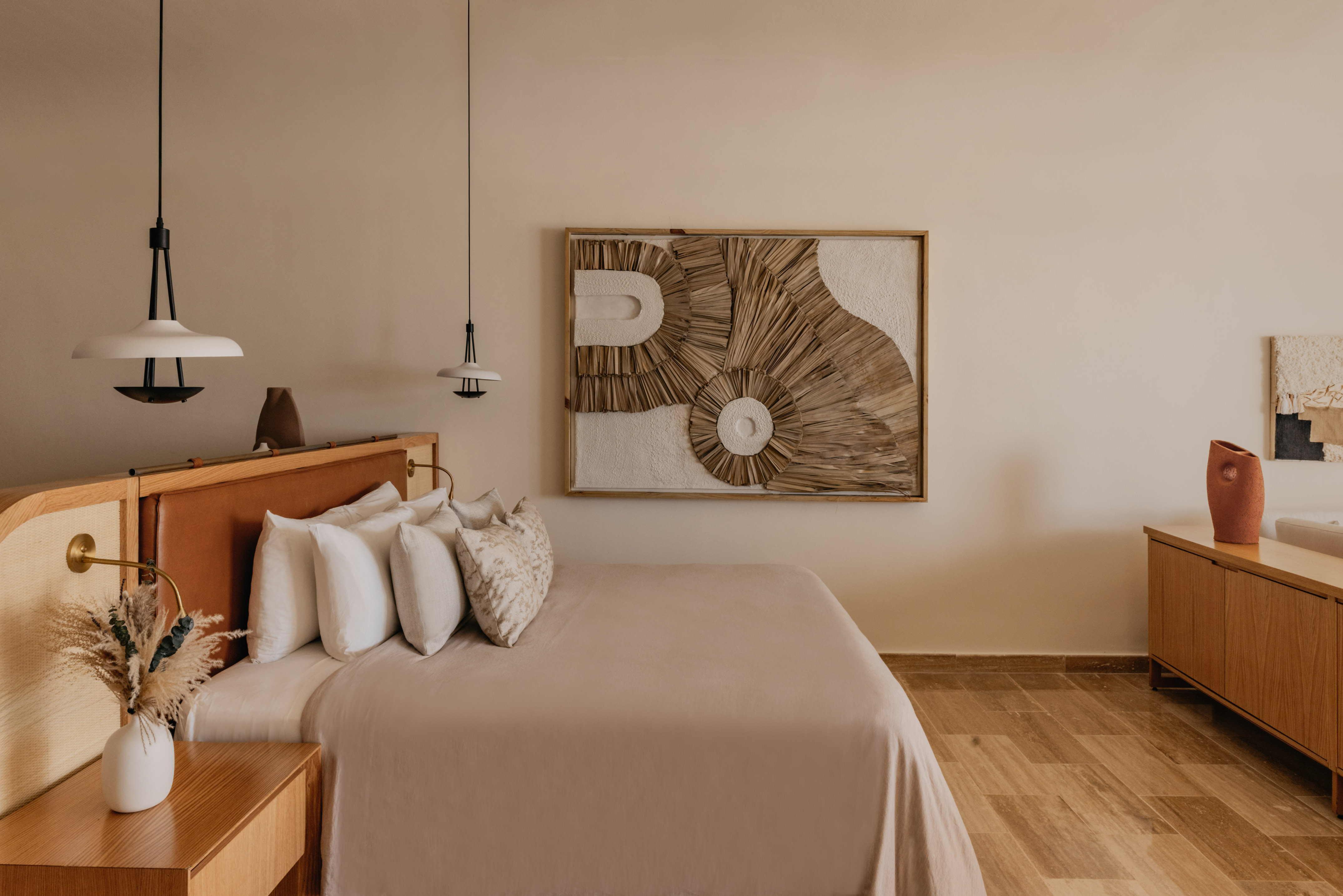 Modern boho bedroom with woven wall art, leather headboard, wood furniture.