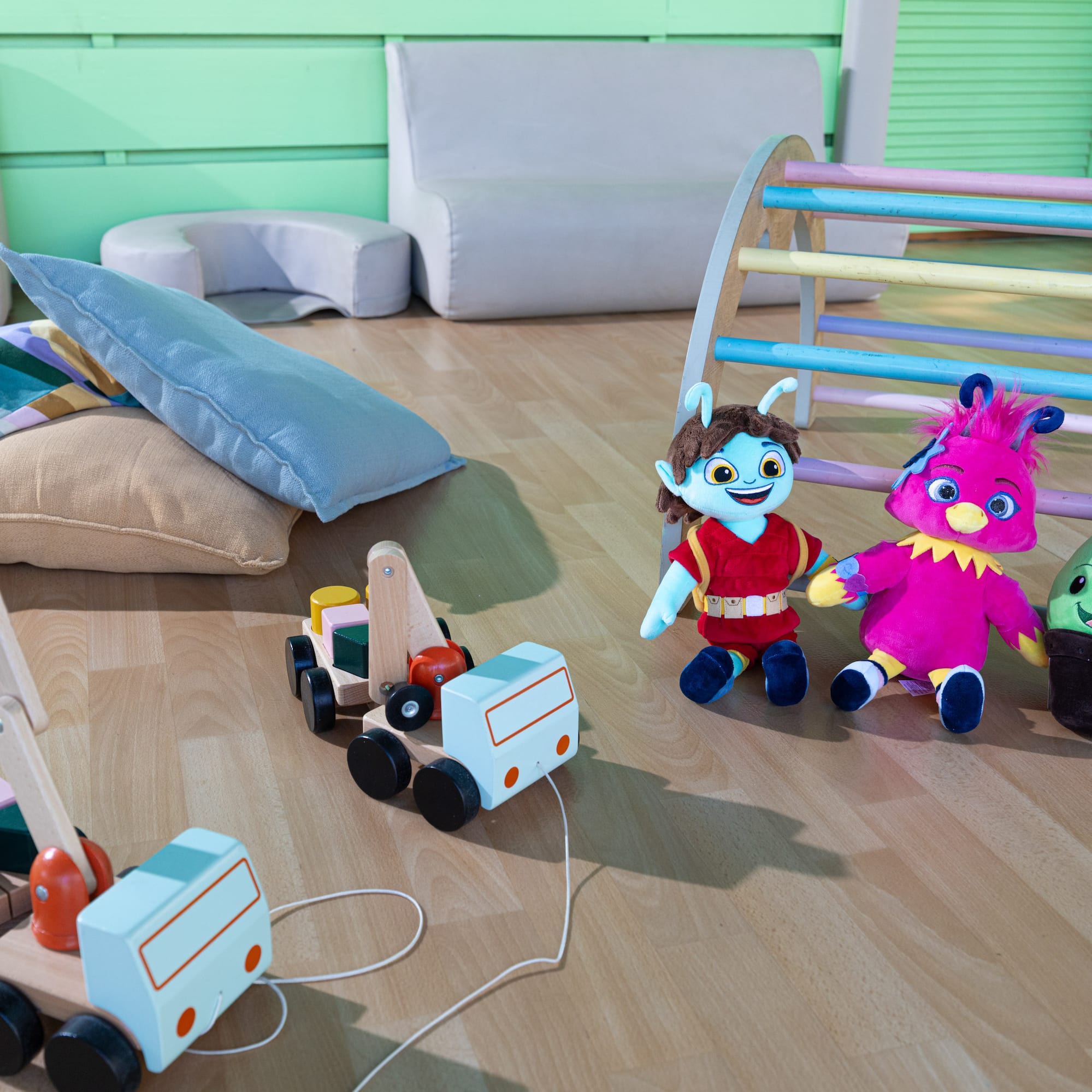 Colorful plush toys, wooden pull-along truck and crane, play gym in a kids' playroom.