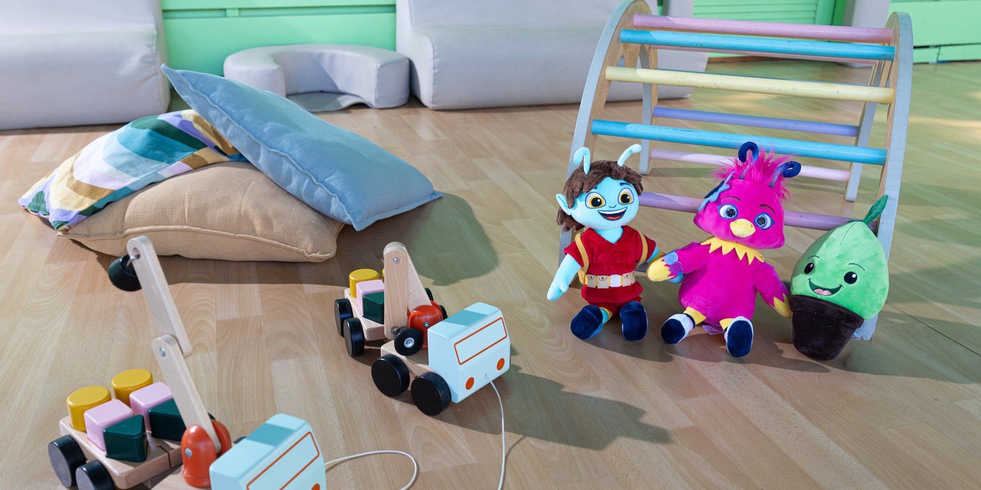 Colorful plush toys, wooden pull-along truck and crane, play gym in a kids' playroom.