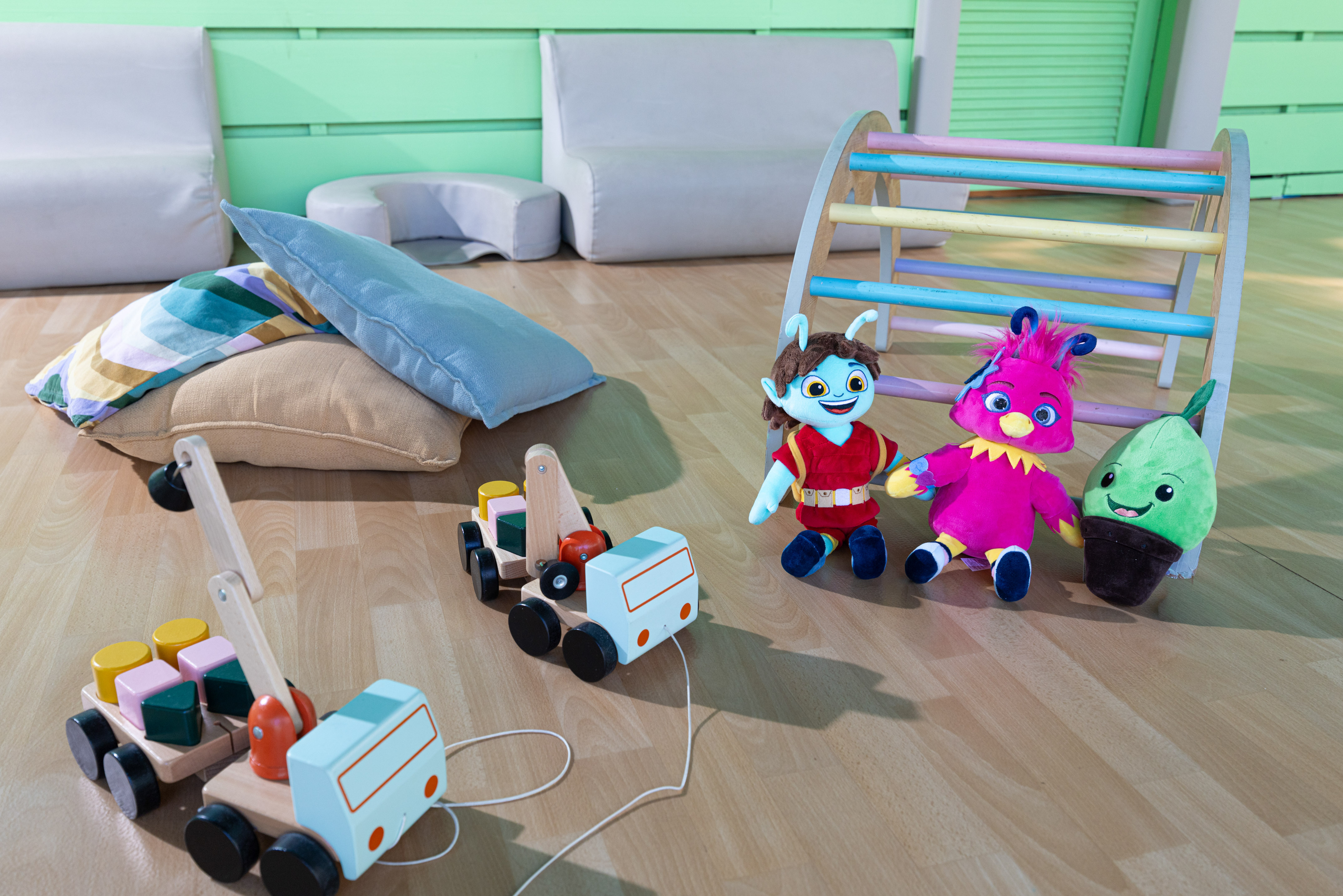 Colorful plush toys, wooden pull-along truck and crane, play gym in a kids' playroom.