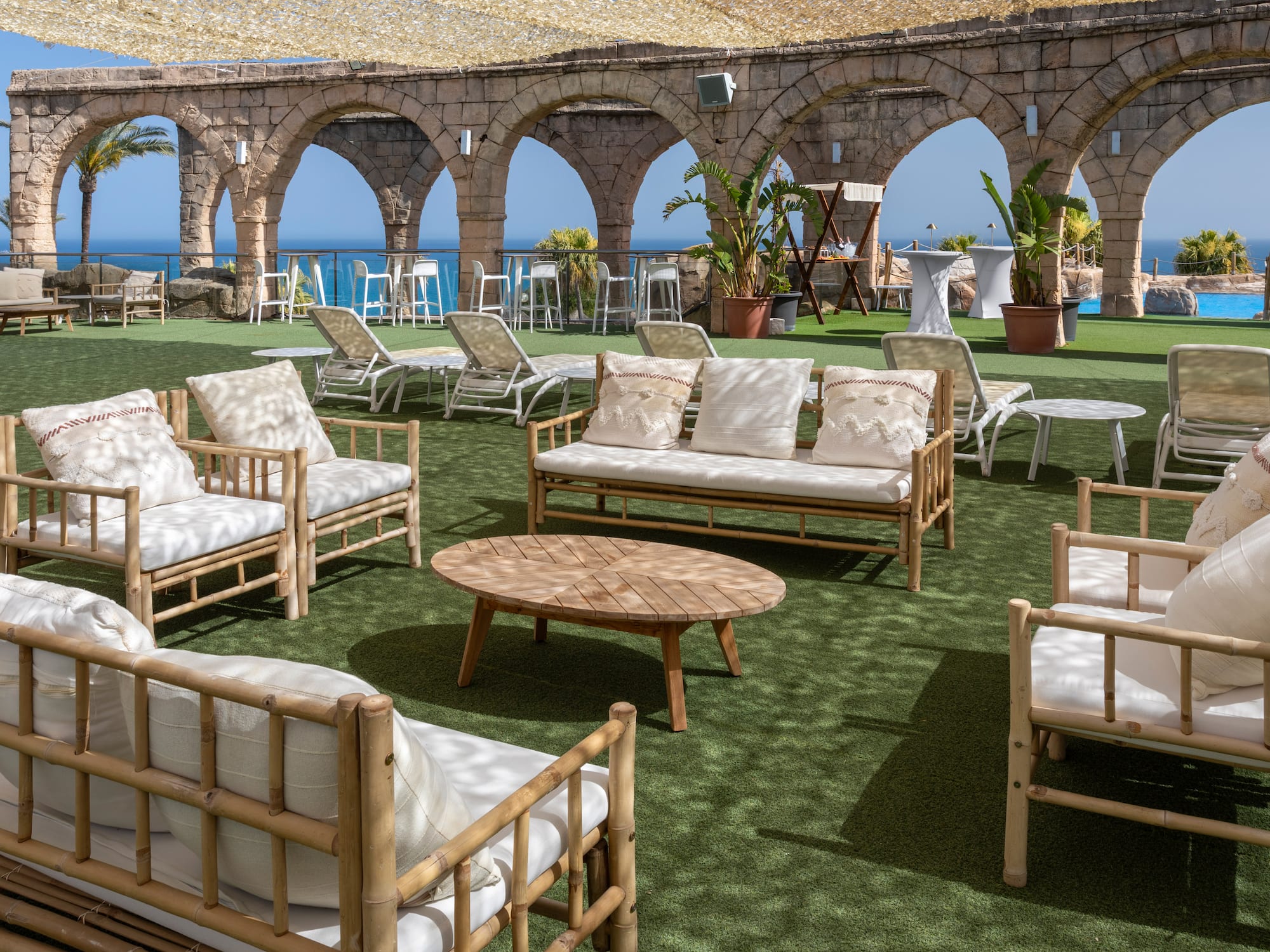 Terrace lounge with bamboo seating, ocean view, stone arches, and artificial turf.