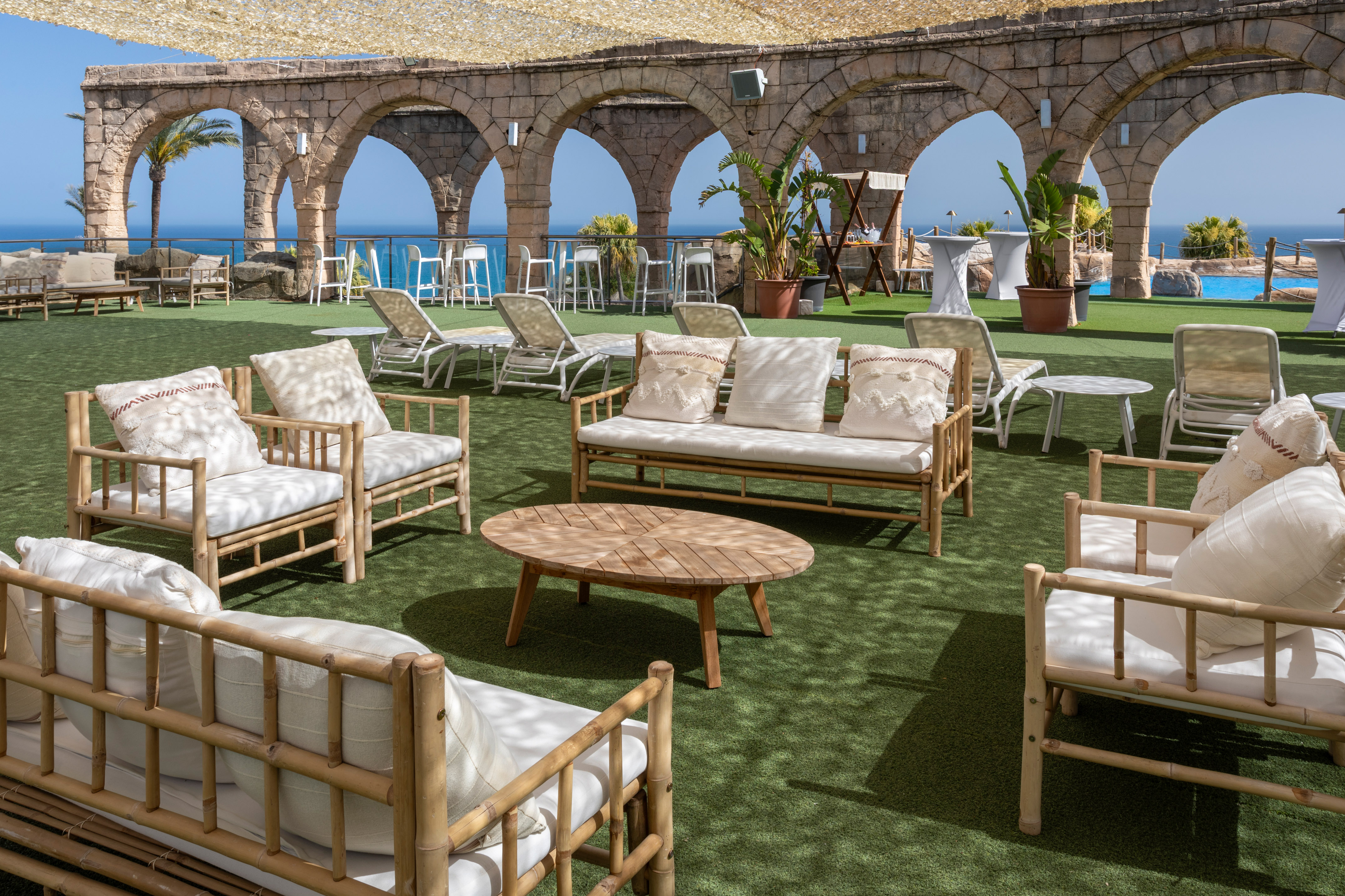 Terrace lounge with bamboo seating, ocean view, stone arches, and artificial turf.