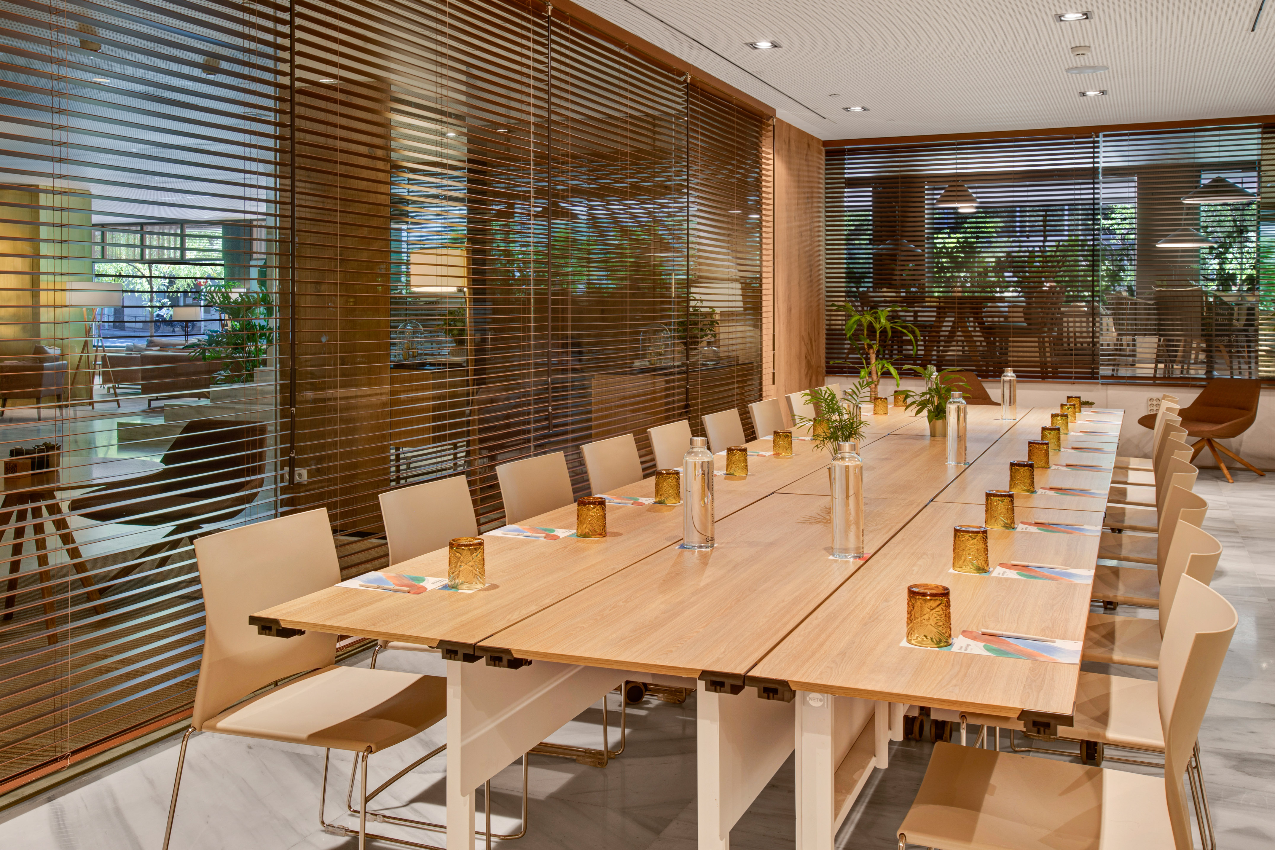 Modern meeting room with long wooden table, beige chairs, and window blinds.
